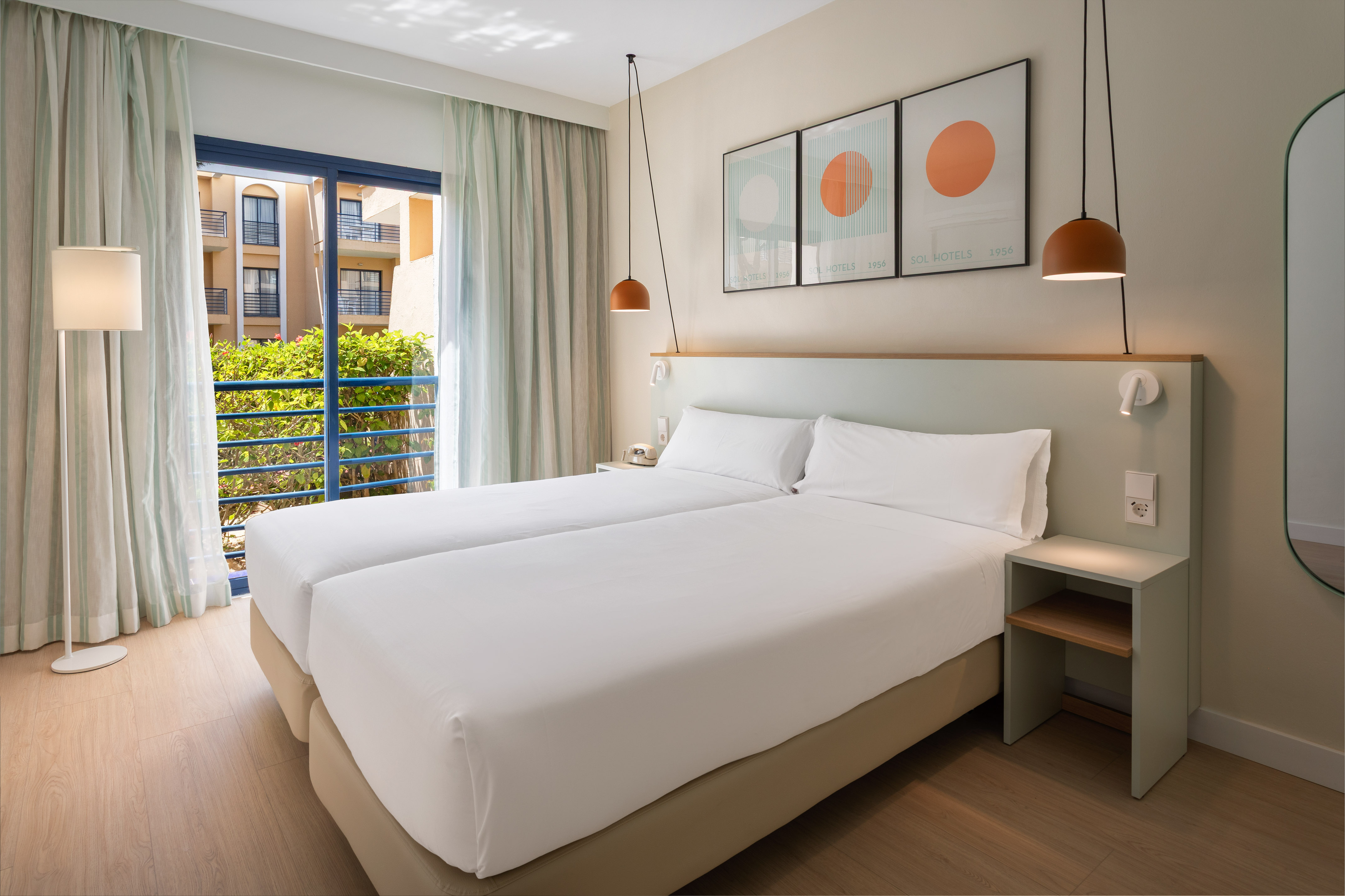 Modern hotel room with two beds, balcony, green headboard, and warm lighting.
