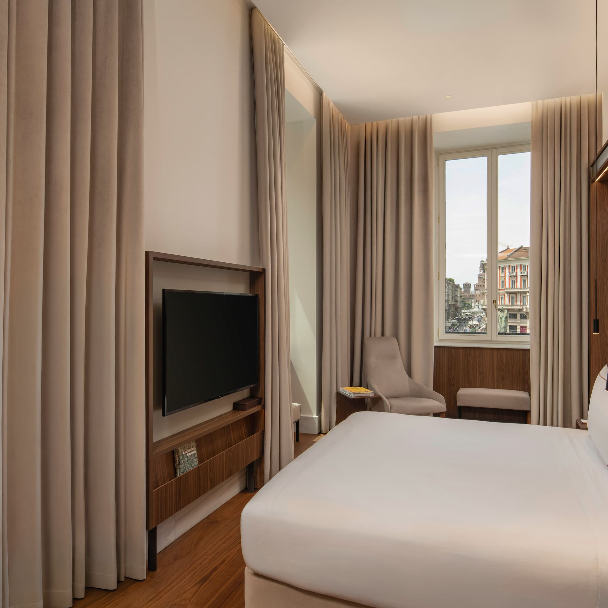Modern hotel room with king bed, city view, wood floors, and wall-mounted TV.