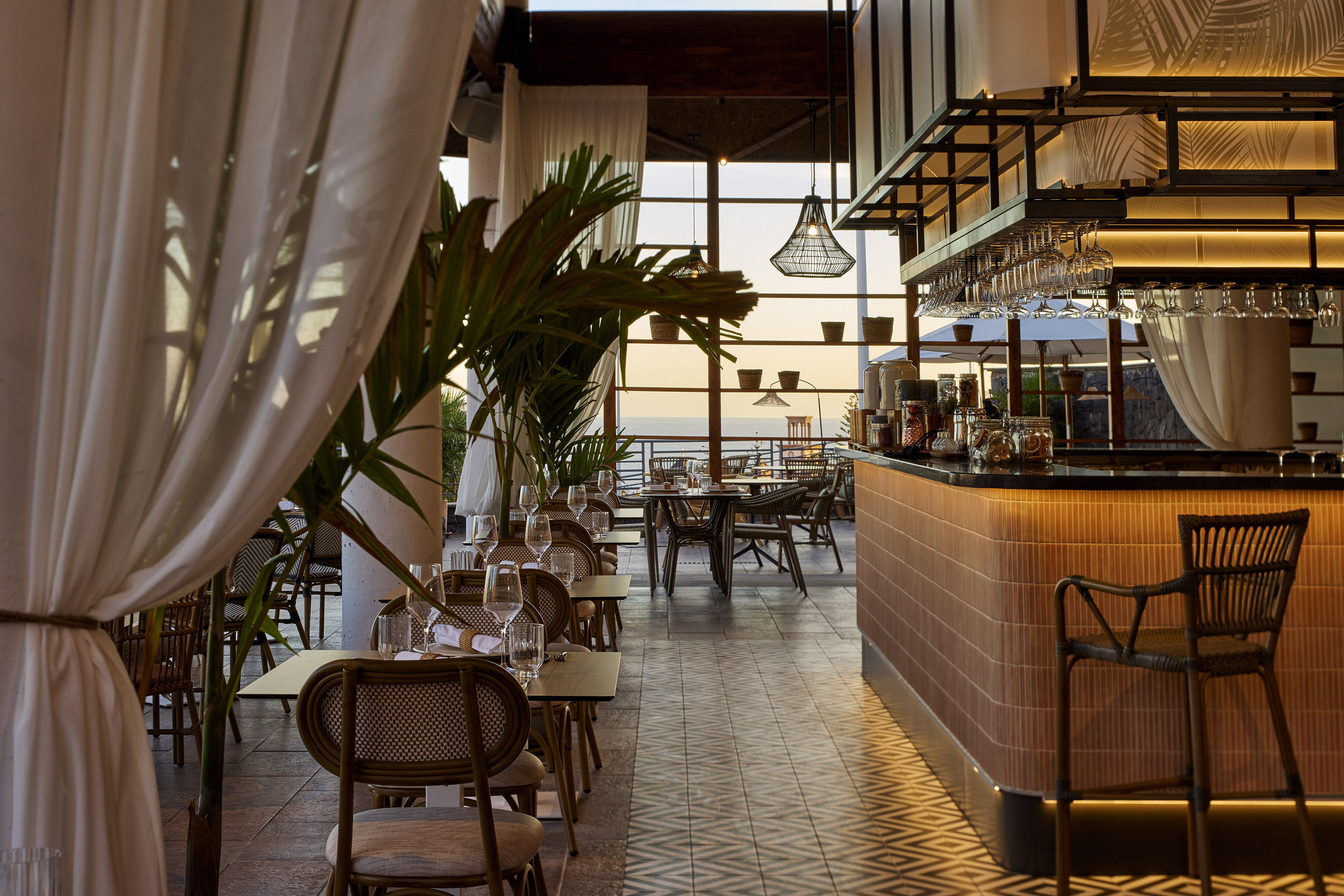 Chic restaurant bar overlooking ocean at sunset with outdoor tables.