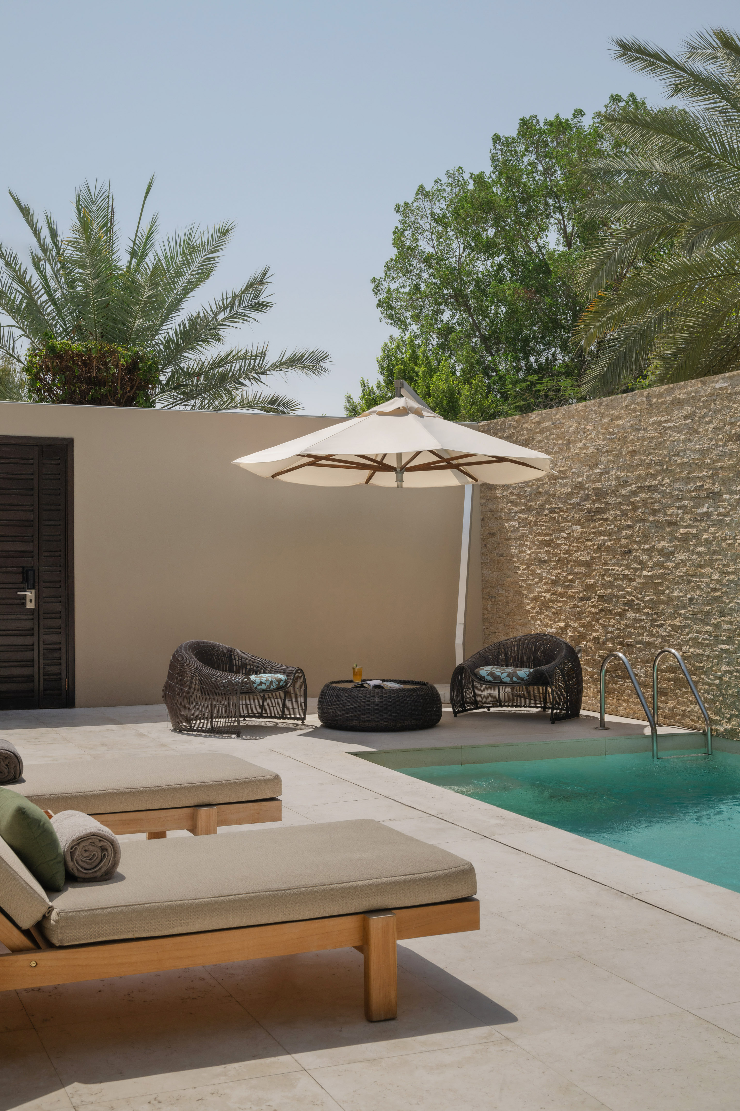 Private pool patio with lounge chairs, umbrella, wicker seating, and palm trees.