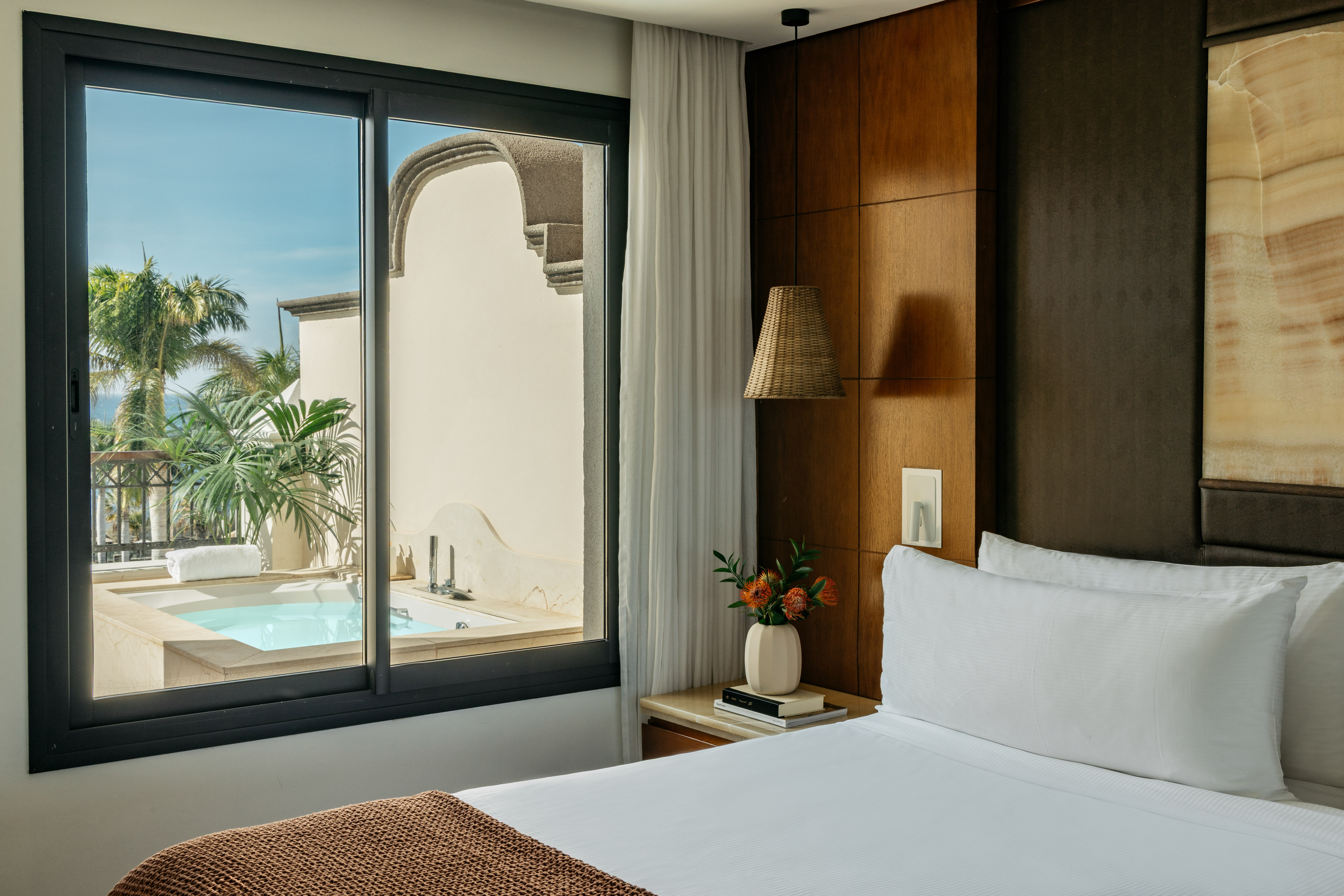Hotel bedroom with window overlooking private hot tub, patio, and palm trees.