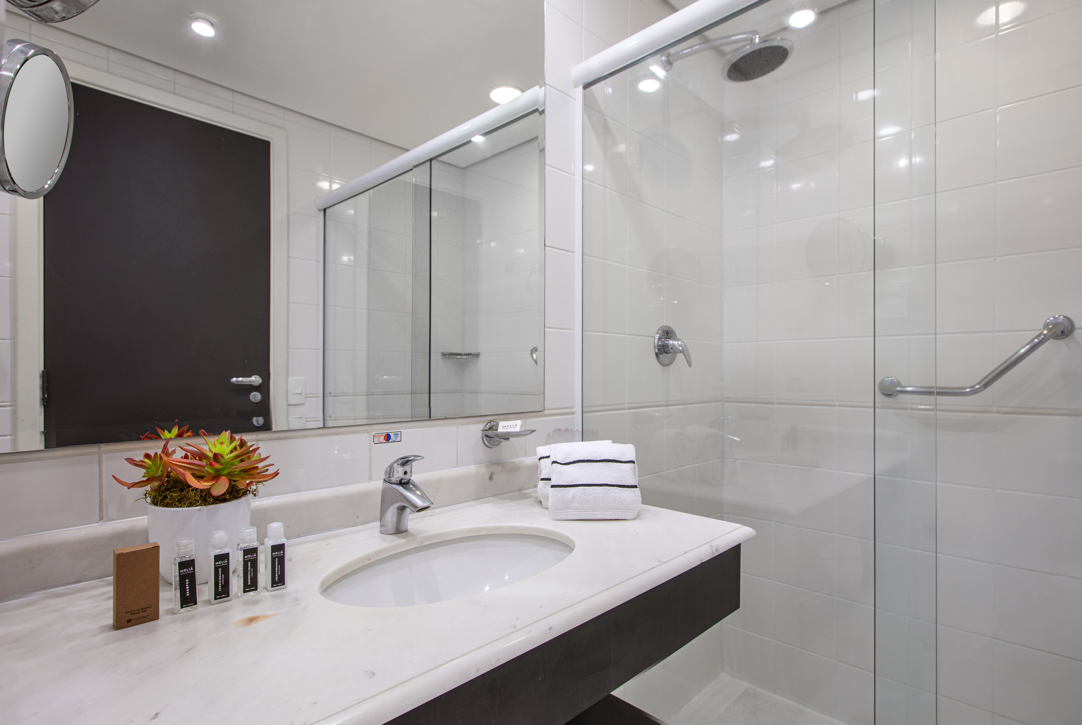 Modern hotel bathroom with marble vanity, glass shower, and amenities.
