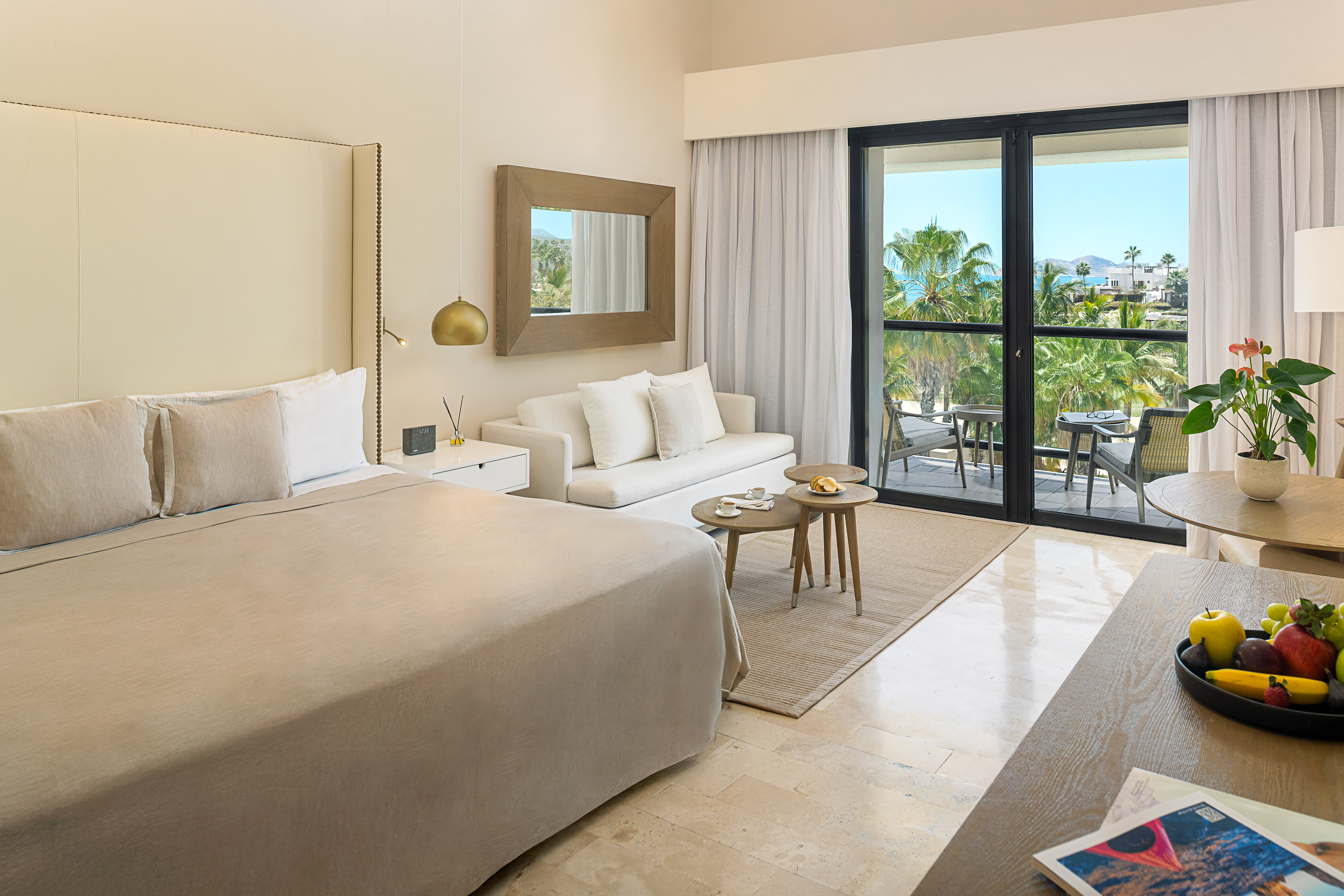 Modern hotel room with king bed, sofa, and balcony offering tropical ocean views.