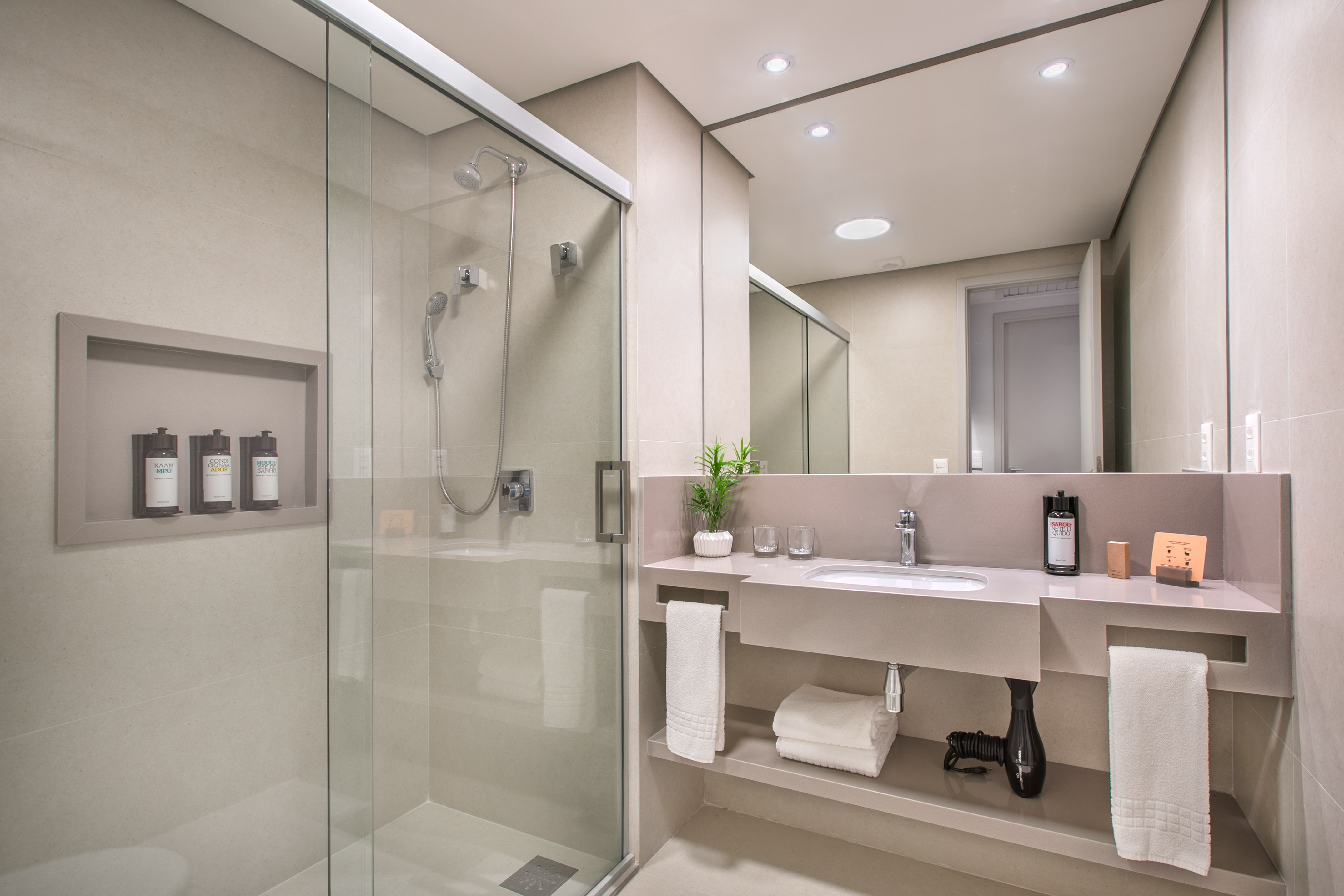 Modern hotel bathroom with glass shower, floating vanity, and mirror.