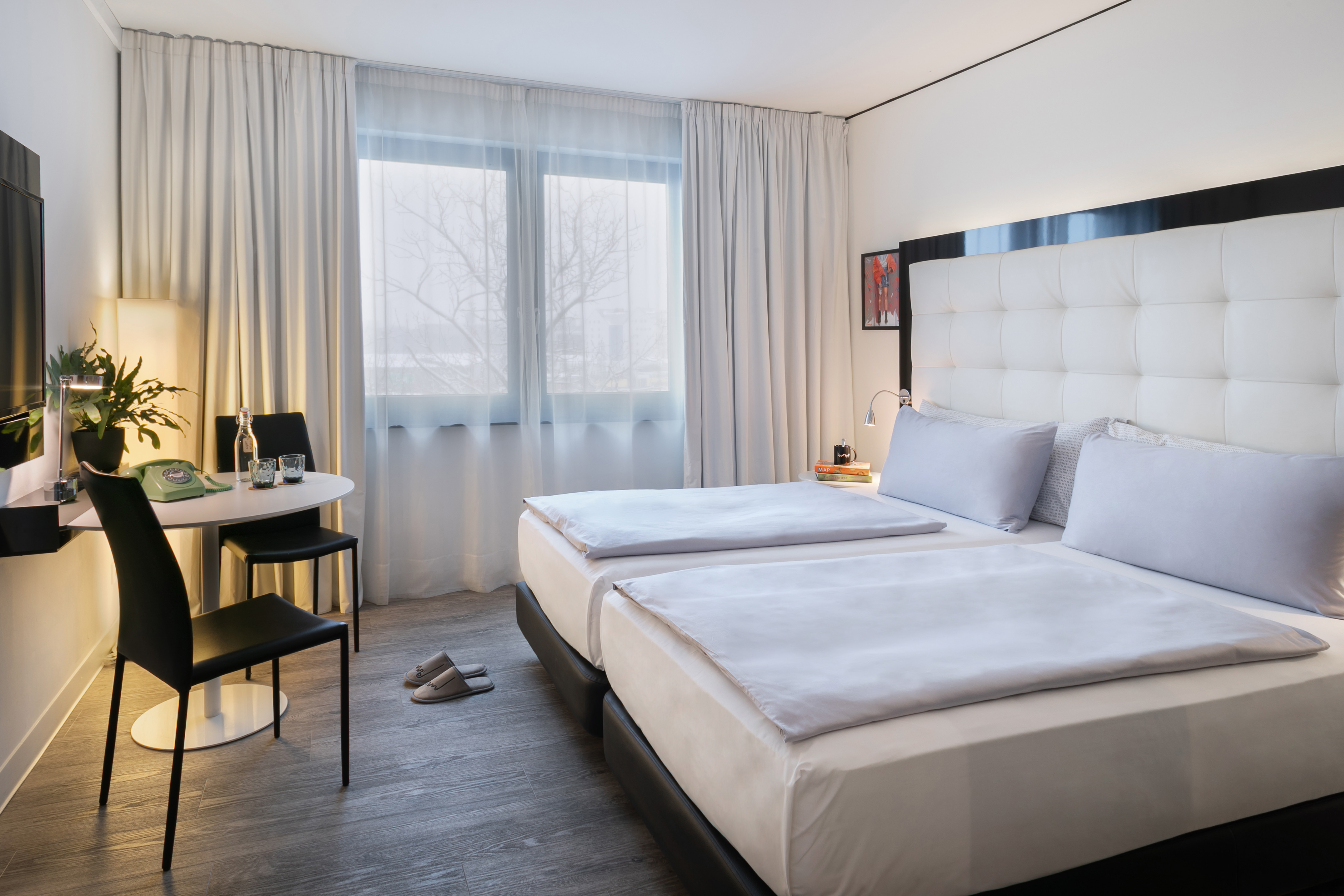 Hotel room with twin beds, white headboard, small table, and window view.