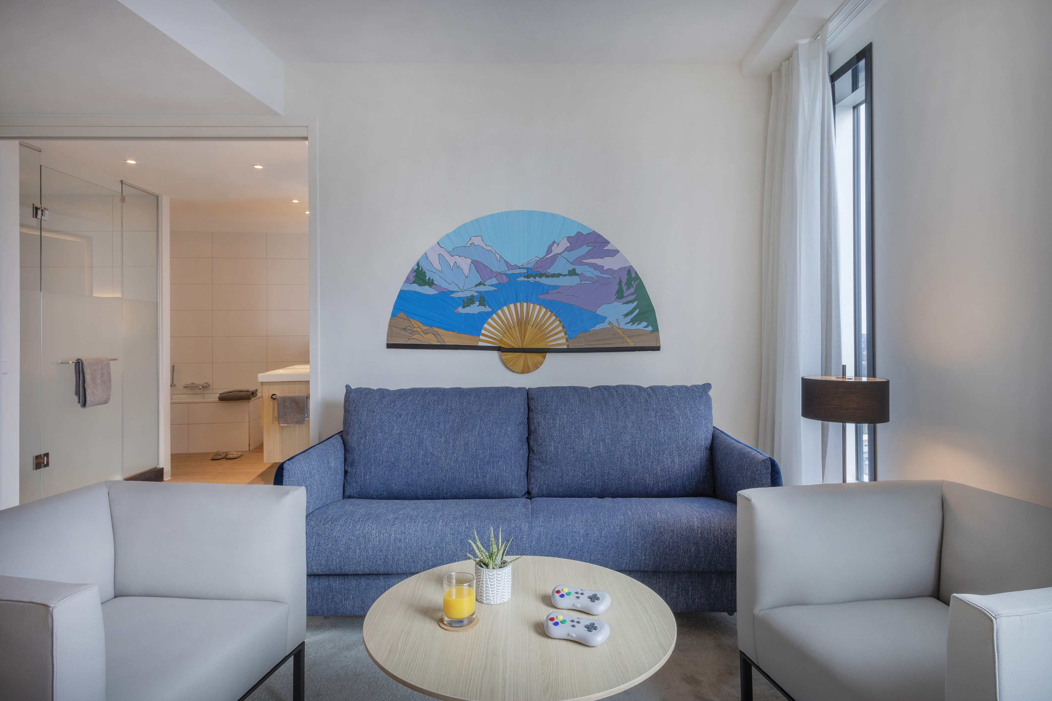 Modern hotel suite living room with blue sofa, coffee table, game controllers.