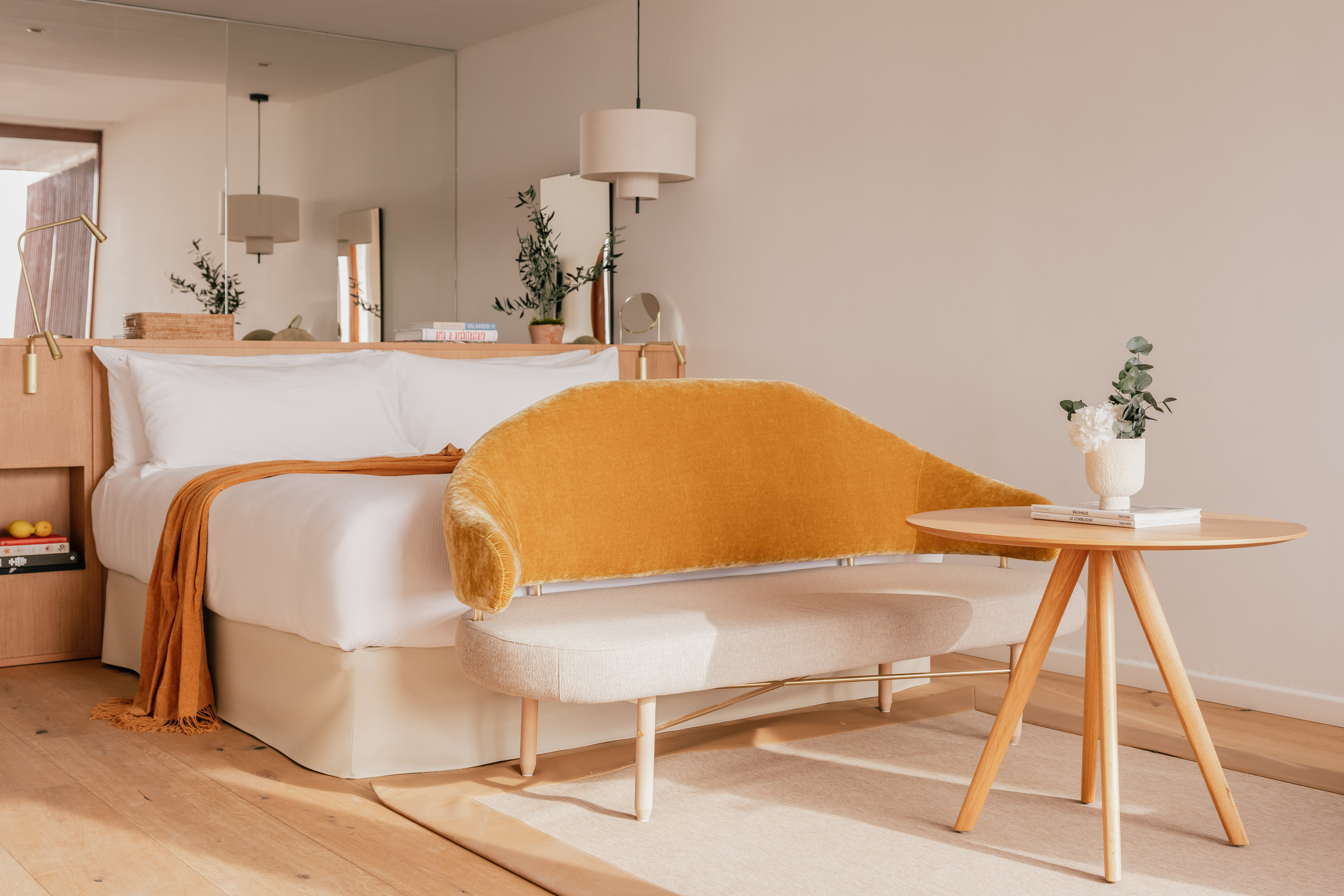 Modern bedroom interior with white bed, yellow velvet bench, and wood accents.