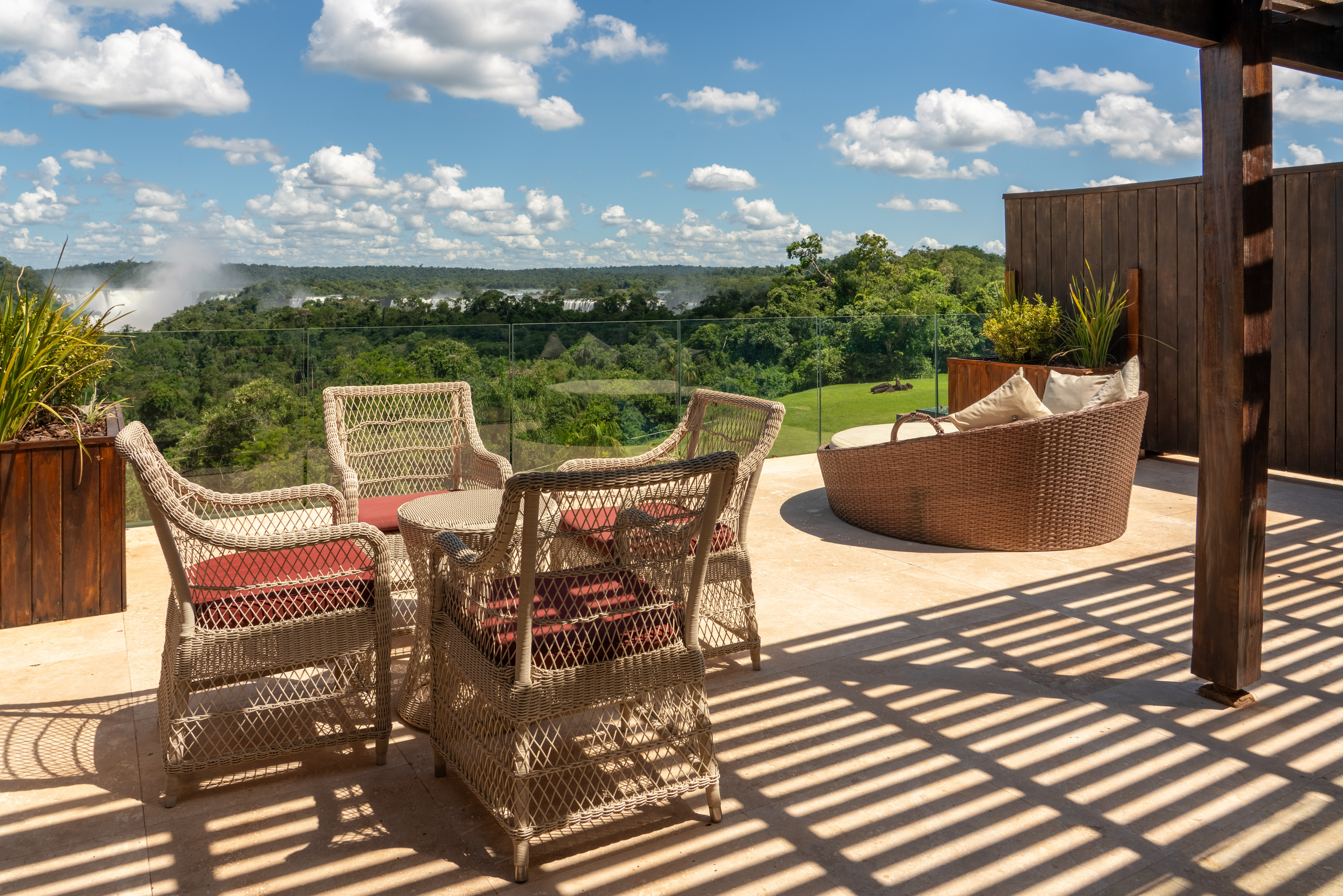 Outdoor patio with wicker furniture, jungle, and distant waterfall mist.