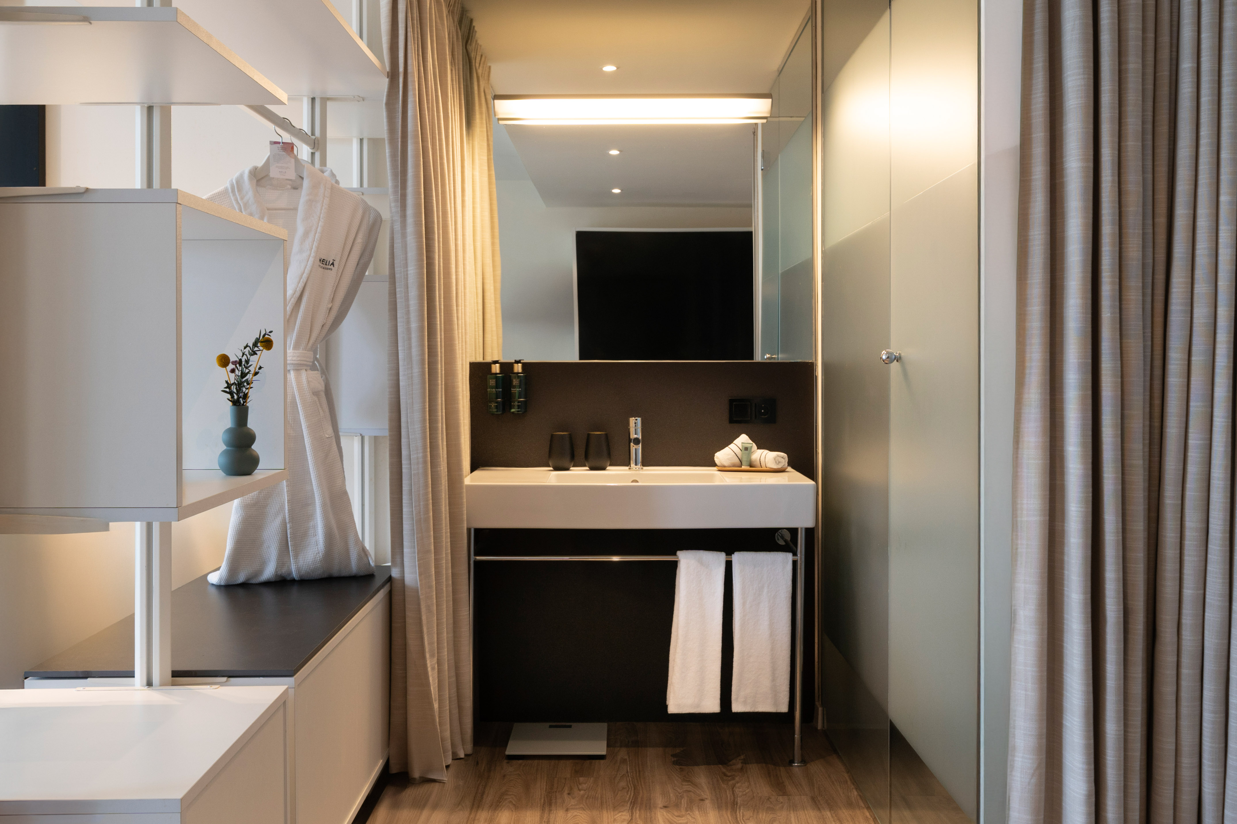 Modern hotel bathroom vanity with sink, mirror, bathrobe, and glass shower.