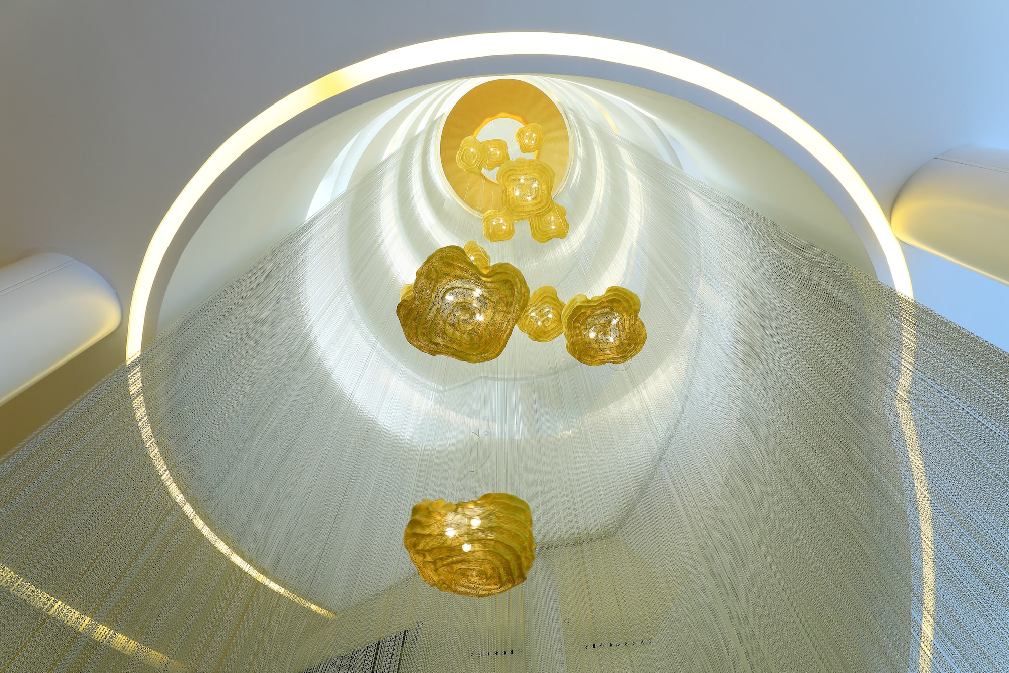 Abstract golden chandeliers in a circular atrium with white chain curtains.