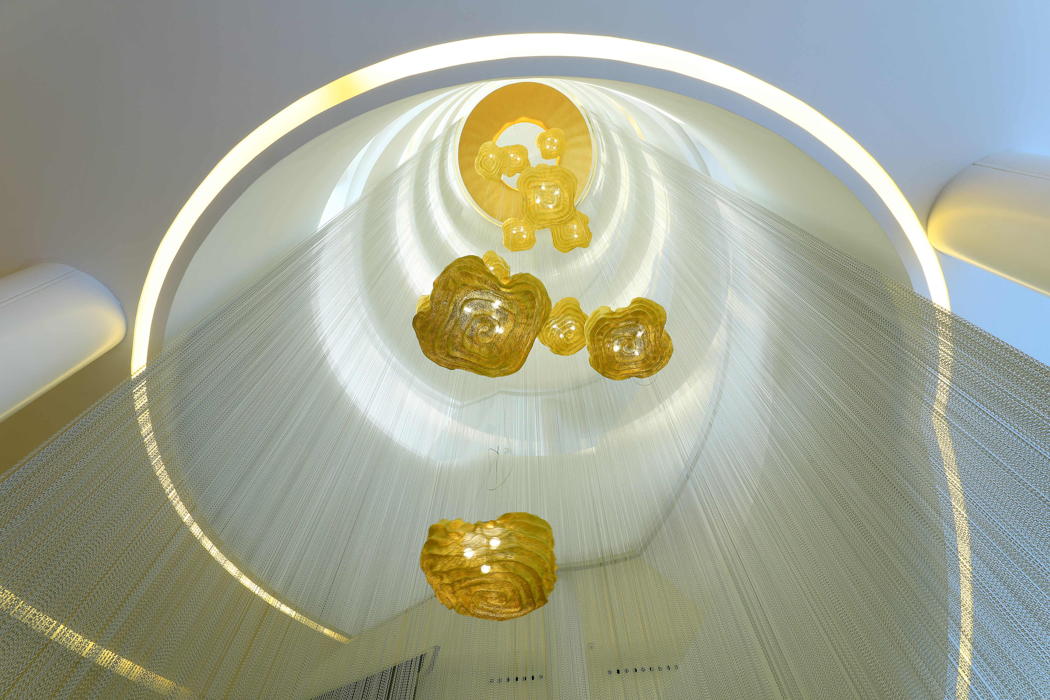 Abstract golden chandeliers in a circular atrium with white chain curtains.