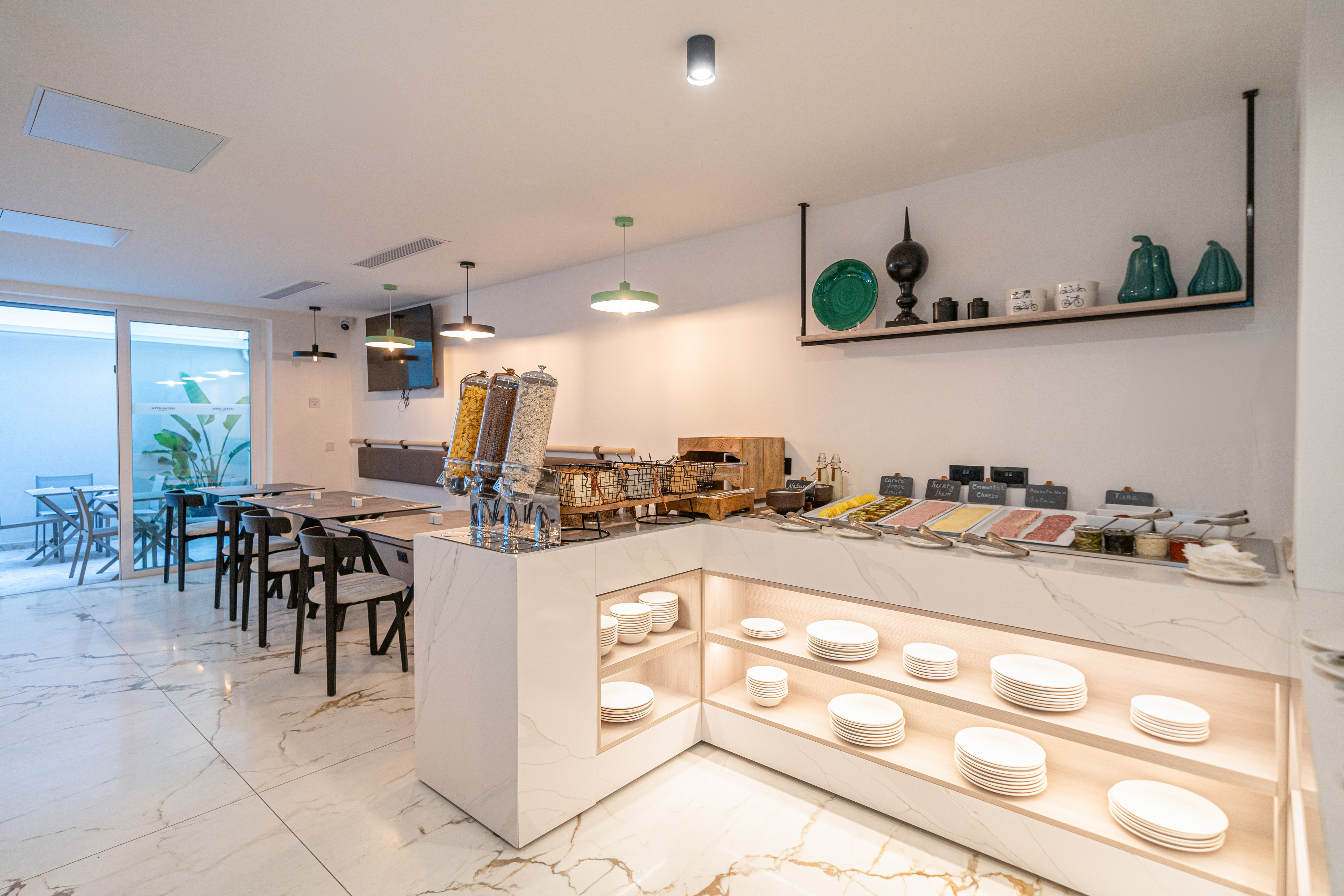 Hotel breakfast buffet with cereals, cold cuts, and modern dining area.