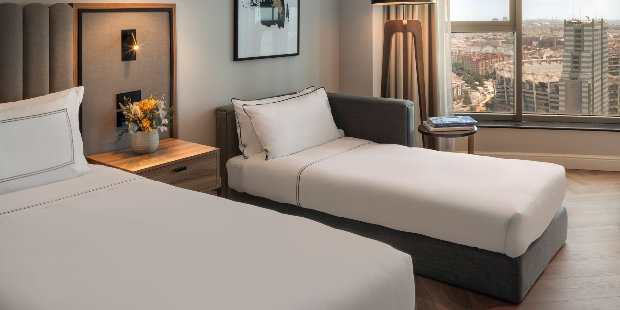 Habitación de hotel moderna con cama, diván y vista panorámica de la ciudad.