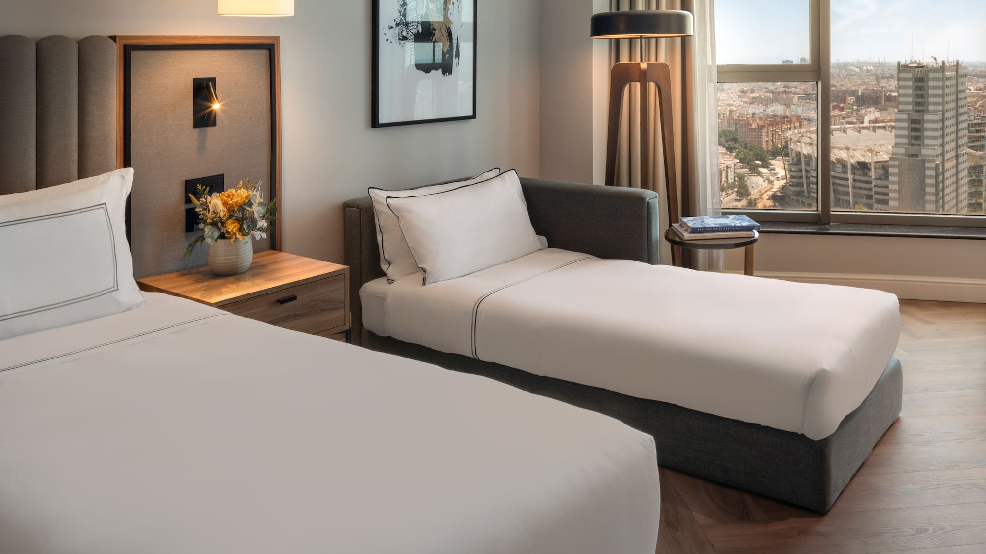 Habitación de hotel moderna con cama, diván y vista panorámica de la ciudad.