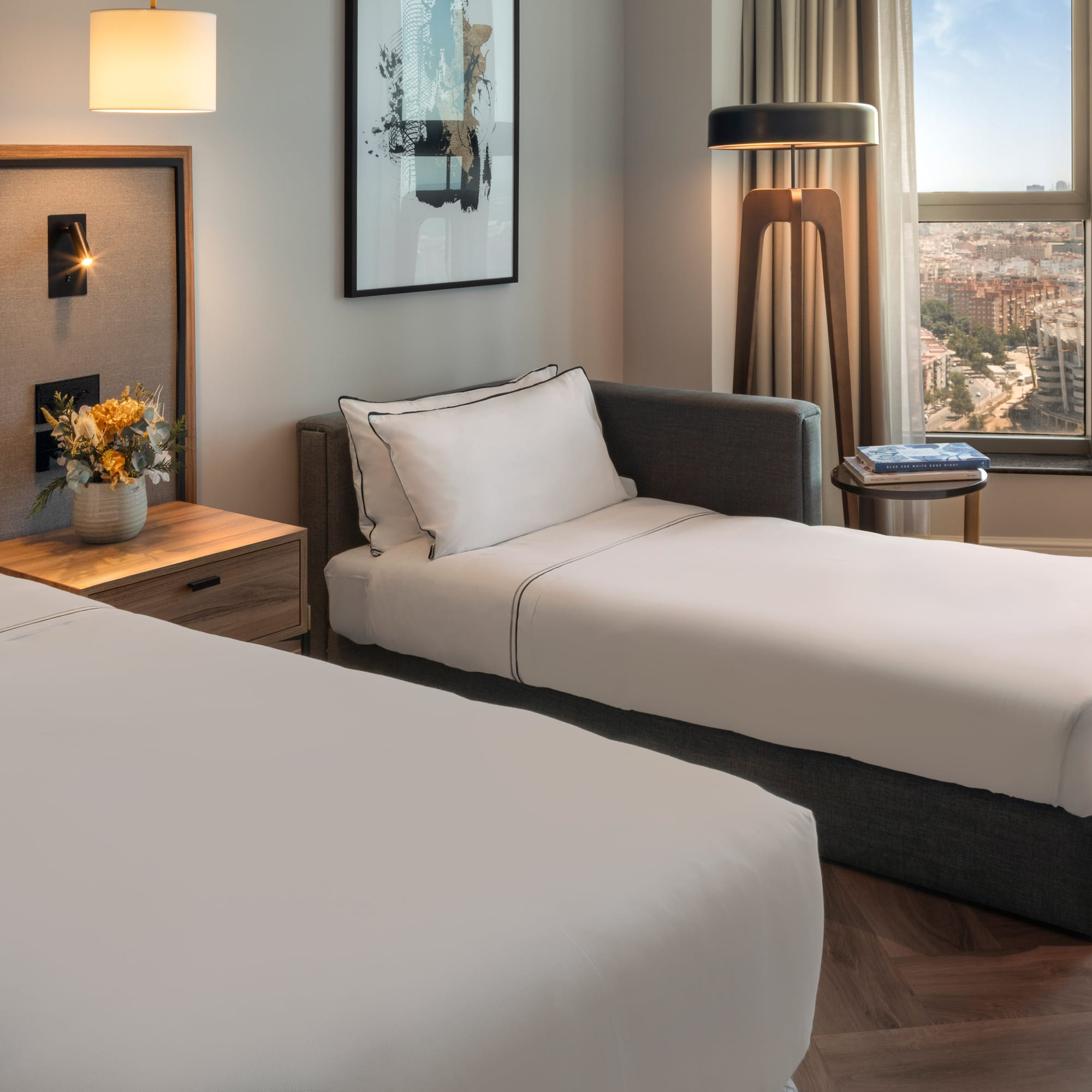 Habitación de hotel moderna con cama, diván, mesita y vistas a la ciudad.