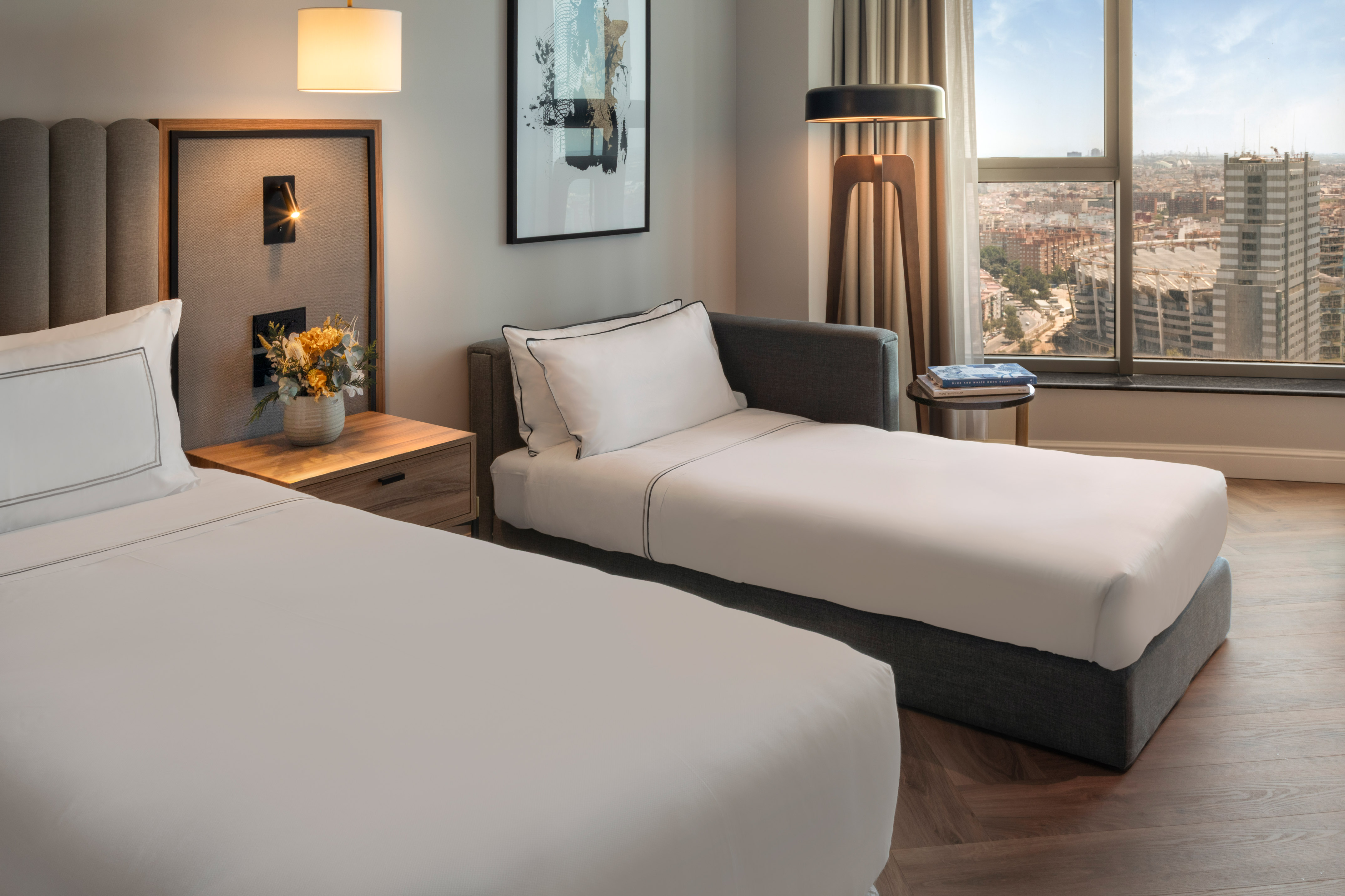 Habitación de hotel moderna con cama, diván, mesita y vistas a la ciudad.