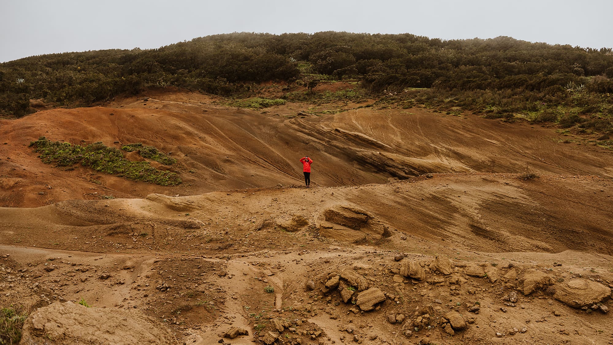 Person in red jacket exploring unique red and brown volcanic landscape.