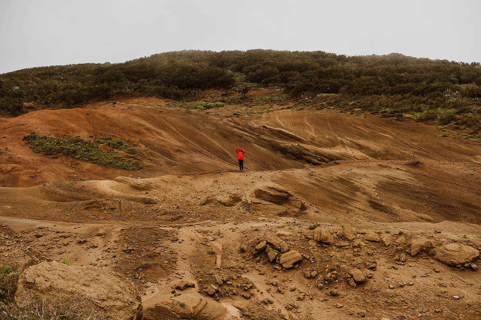 Person in red jacket exploring unique red and brown volcanic landscape.