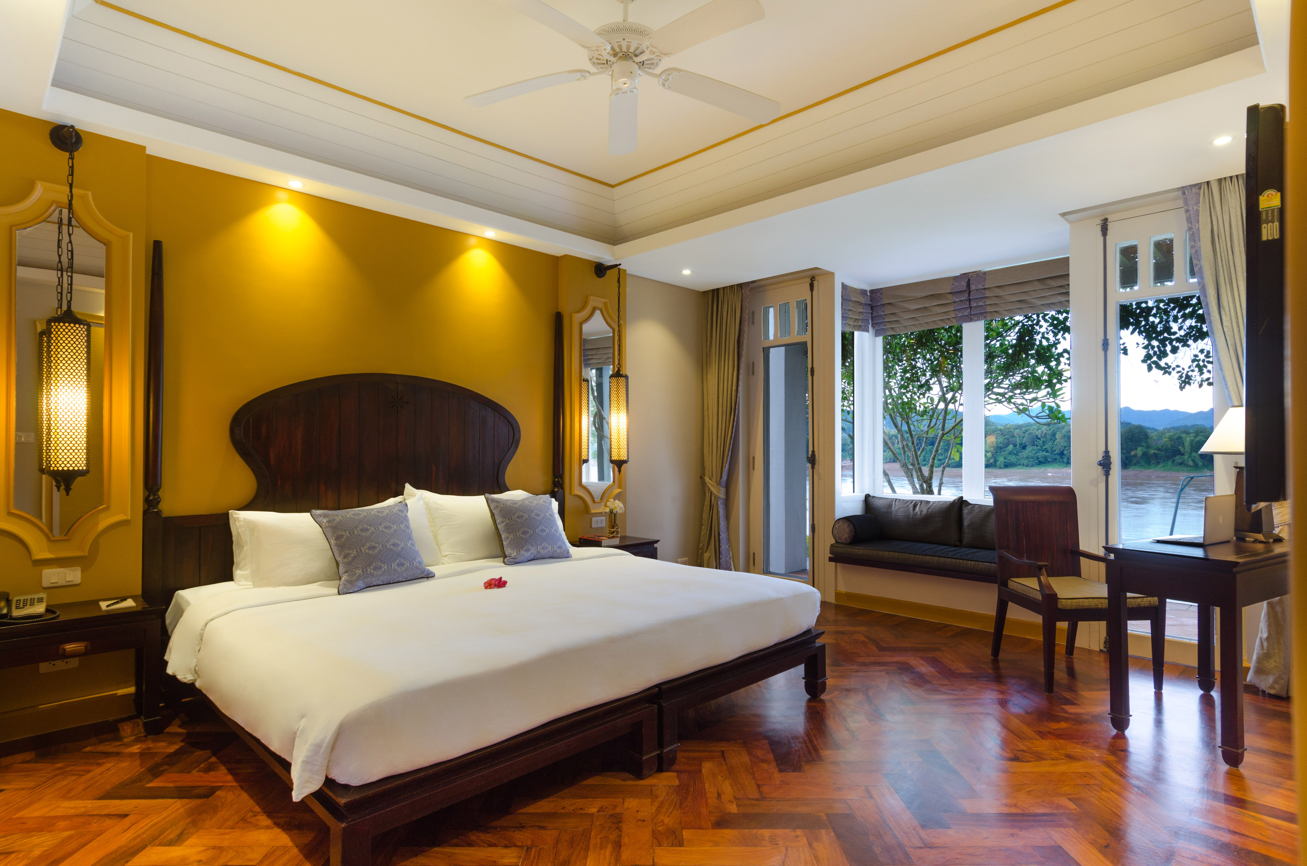 Luxurious hotel bedroom with king bed, golden walls, and scenic river view.