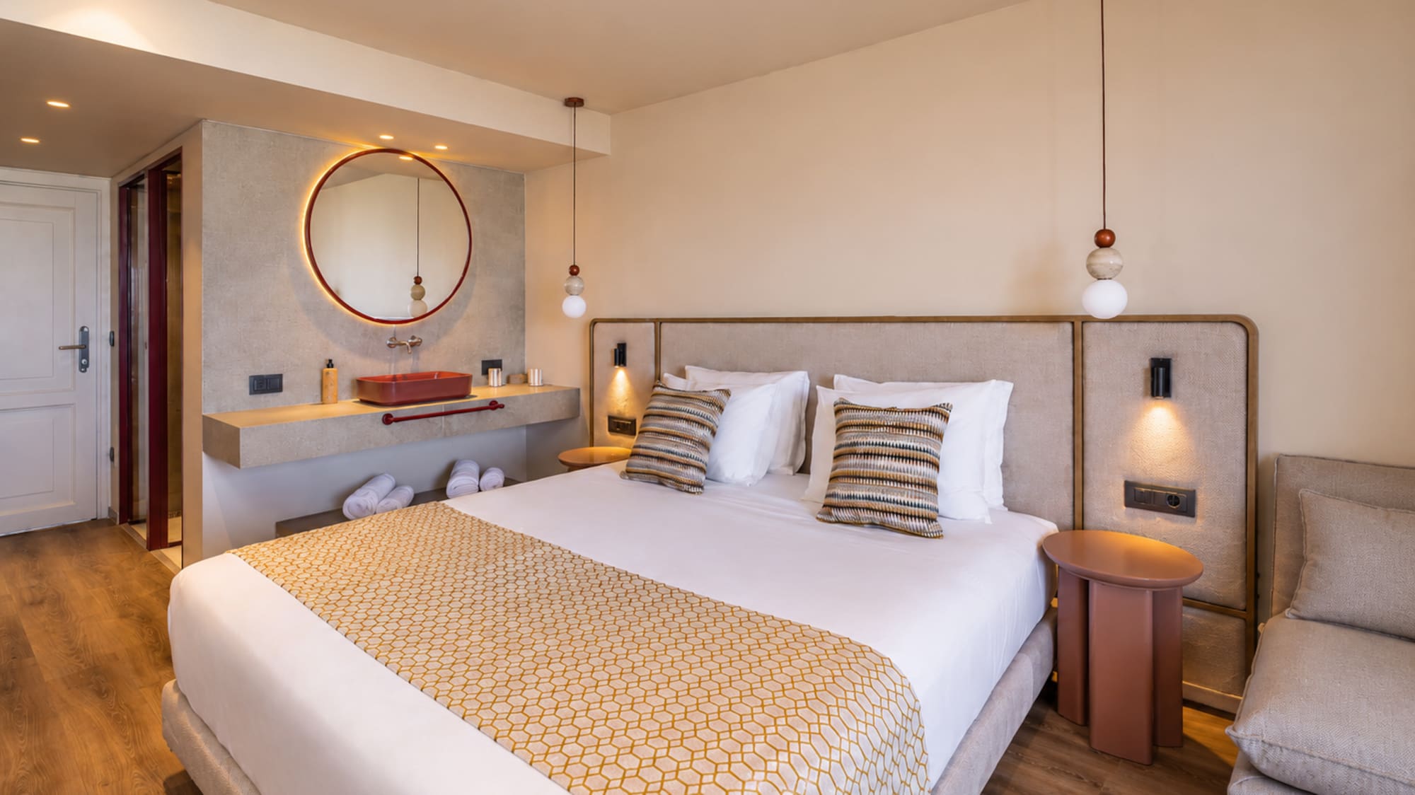 Stylish hotel bedroom featuring a king bed, red vanity, and circular mirror.
