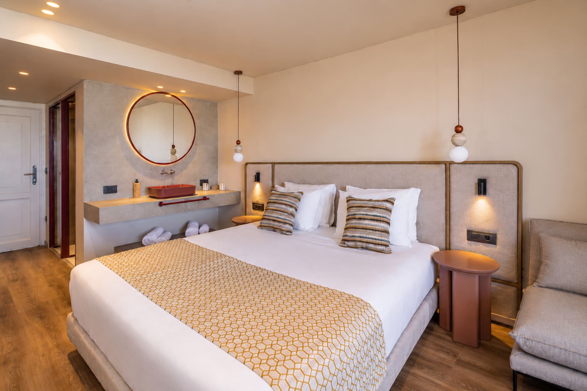 Stylish hotel bedroom featuring a king bed, red vanity, and circular mirror.