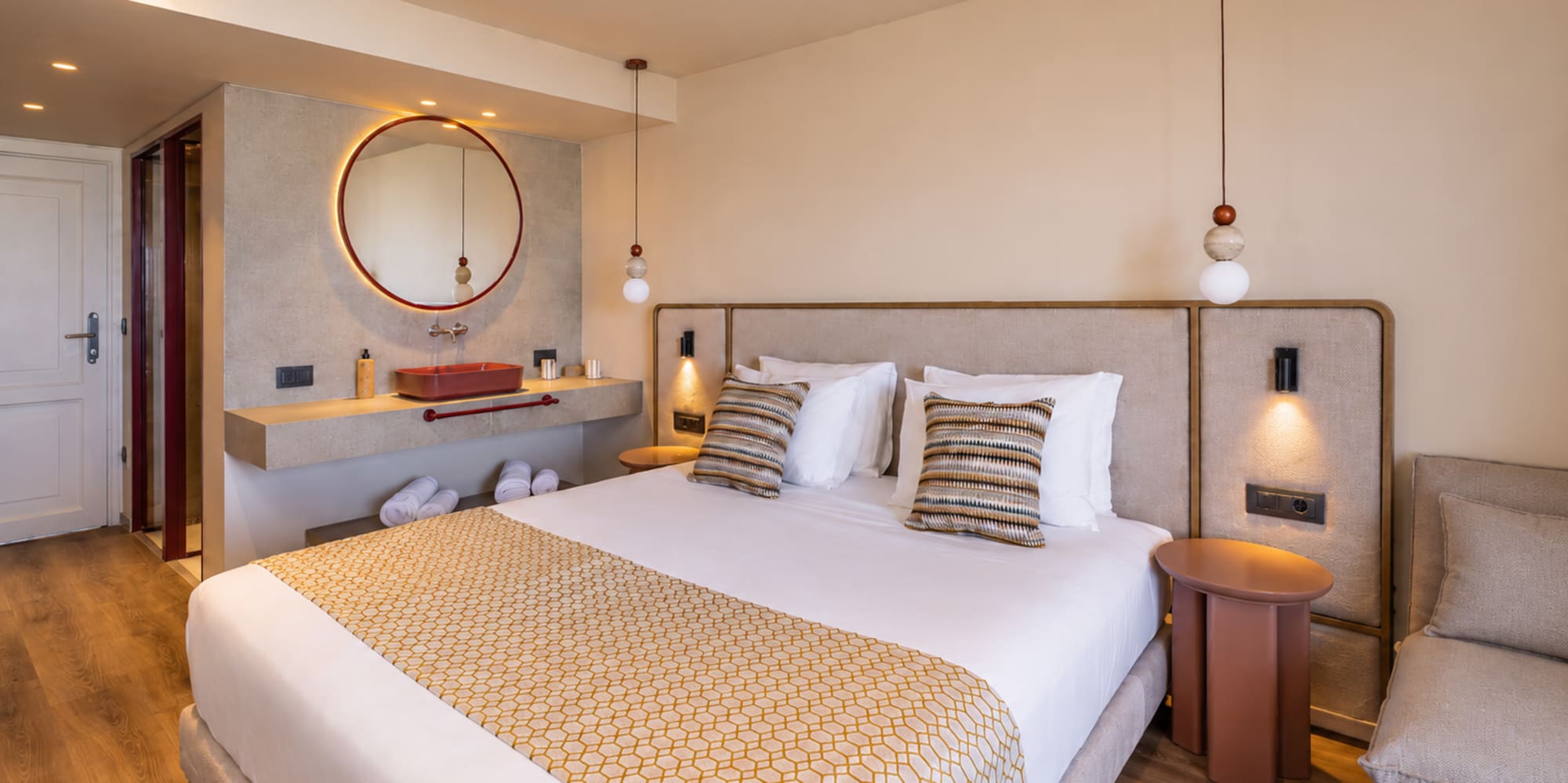 Stylish hotel bedroom featuring a king bed, red vanity, and circular mirror.