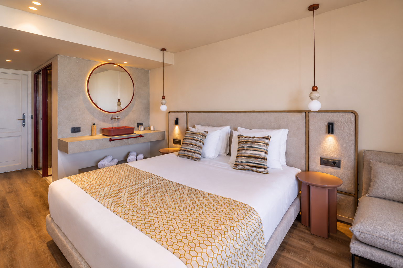 Stylish hotel bedroom featuring a king bed, red vanity, and circular mirror.