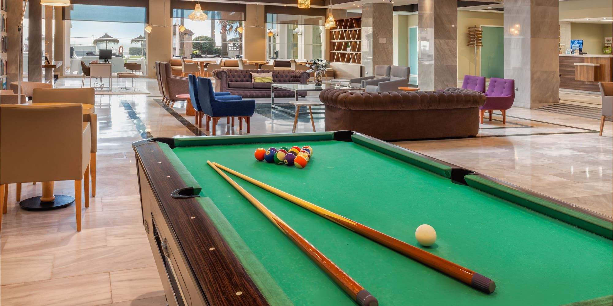 a pool table with cue sticks and balls in a room with a large window