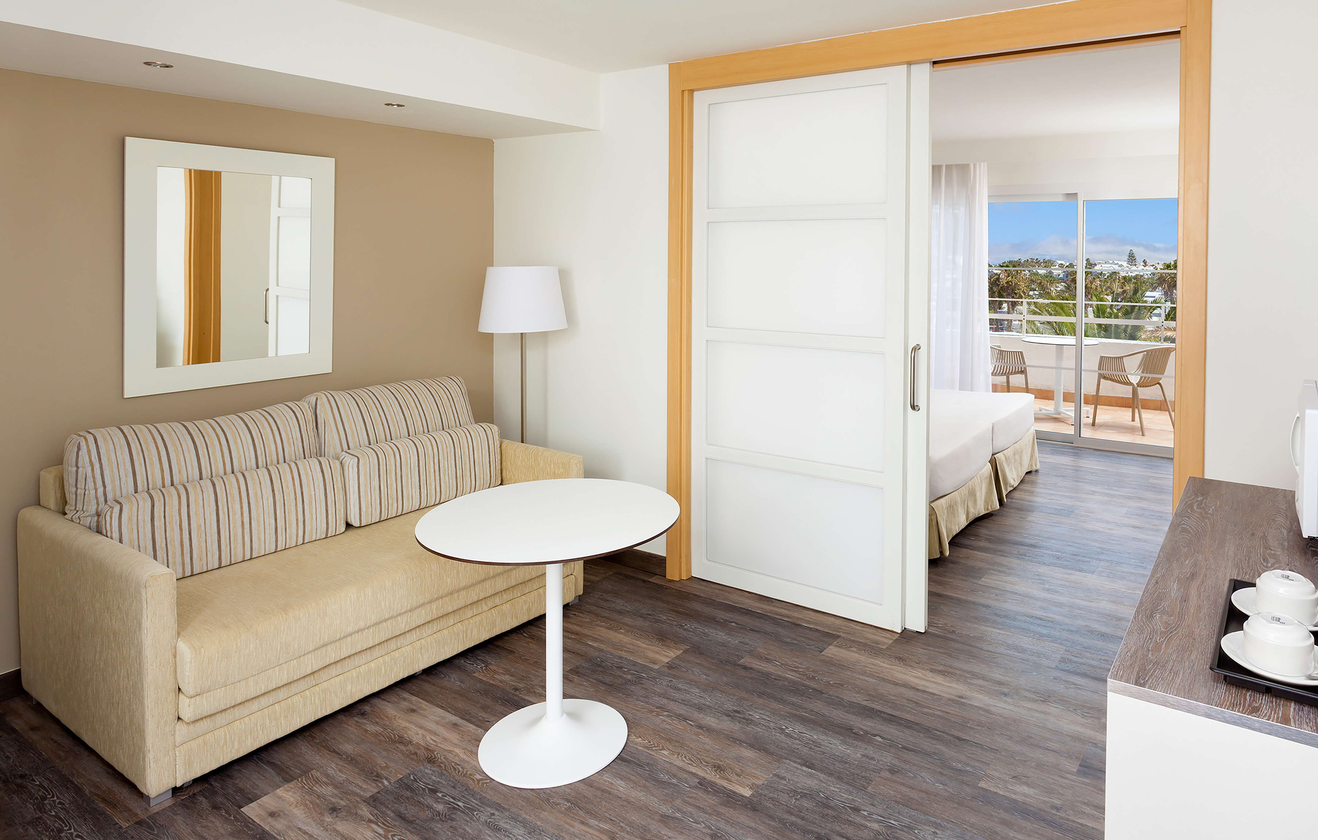 Modern hotel suite with living area, beige sofa, and balcony access.