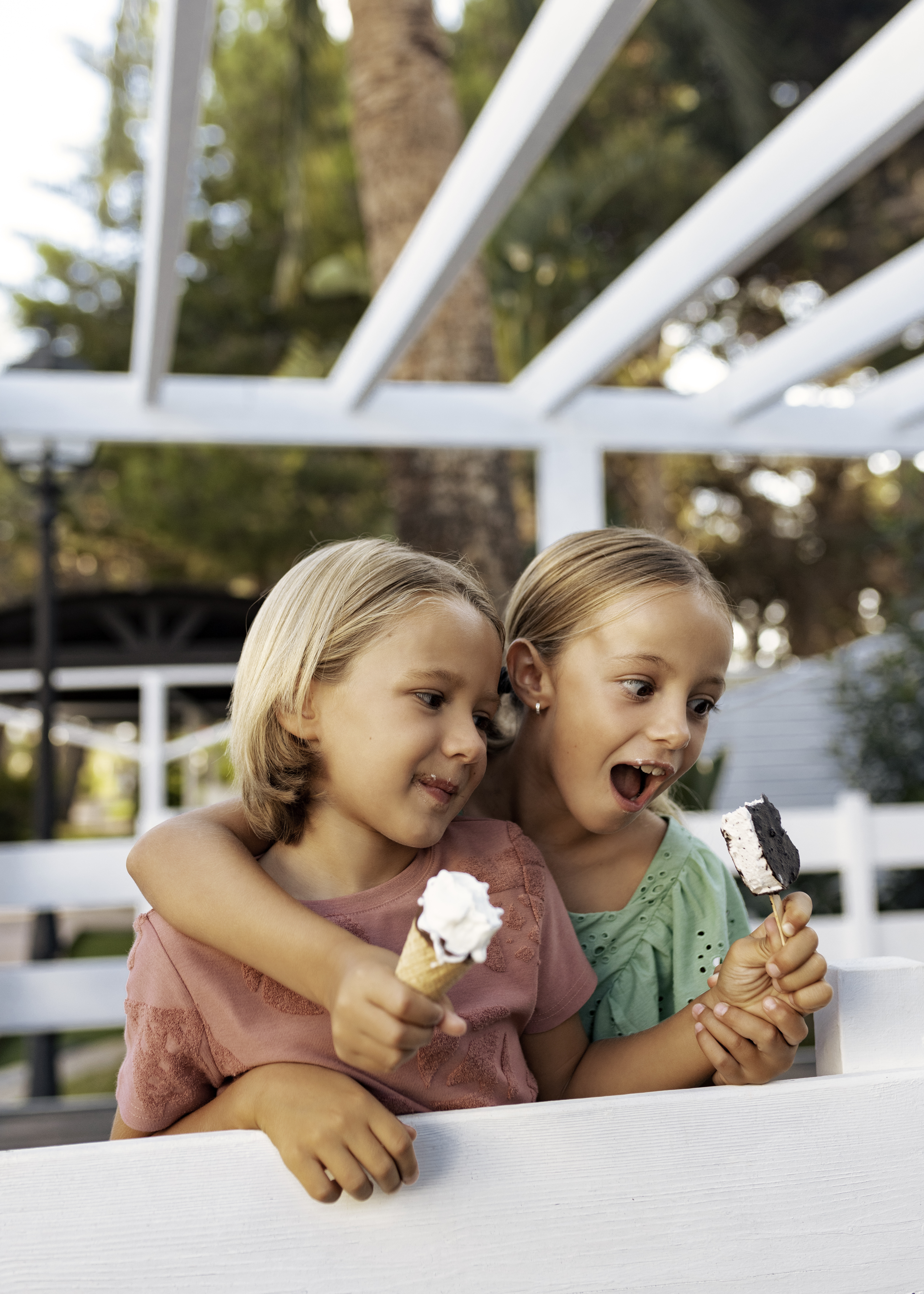 Blonde girls enjoying ice cream cones and bars outdoors.