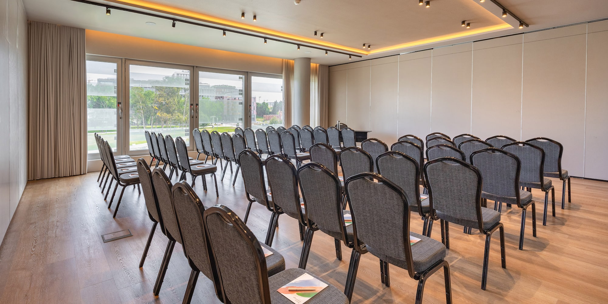 Conference room with chairs, wooden floor, large windows, natural light.