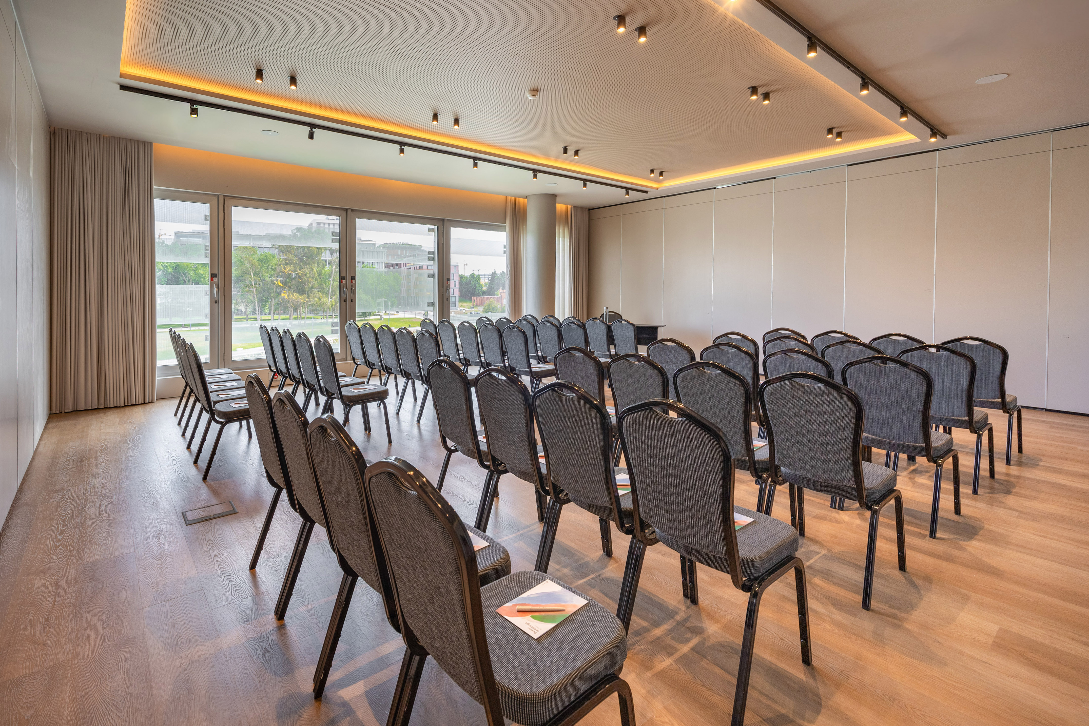Conference room with chairs, wooden floor, large windows, natural light.