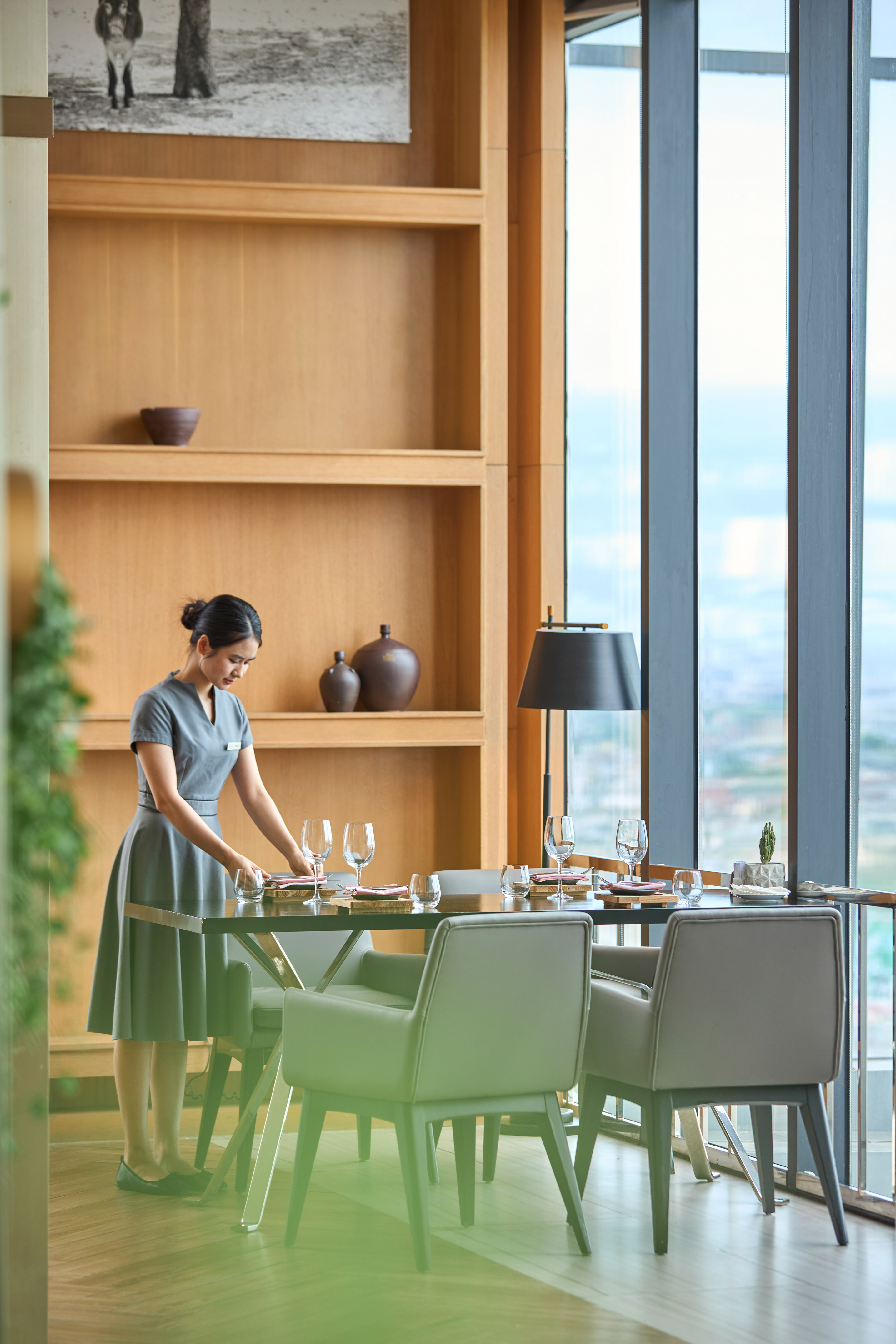 Asian waitress setting a dining table in a modern restaurant with a city view.