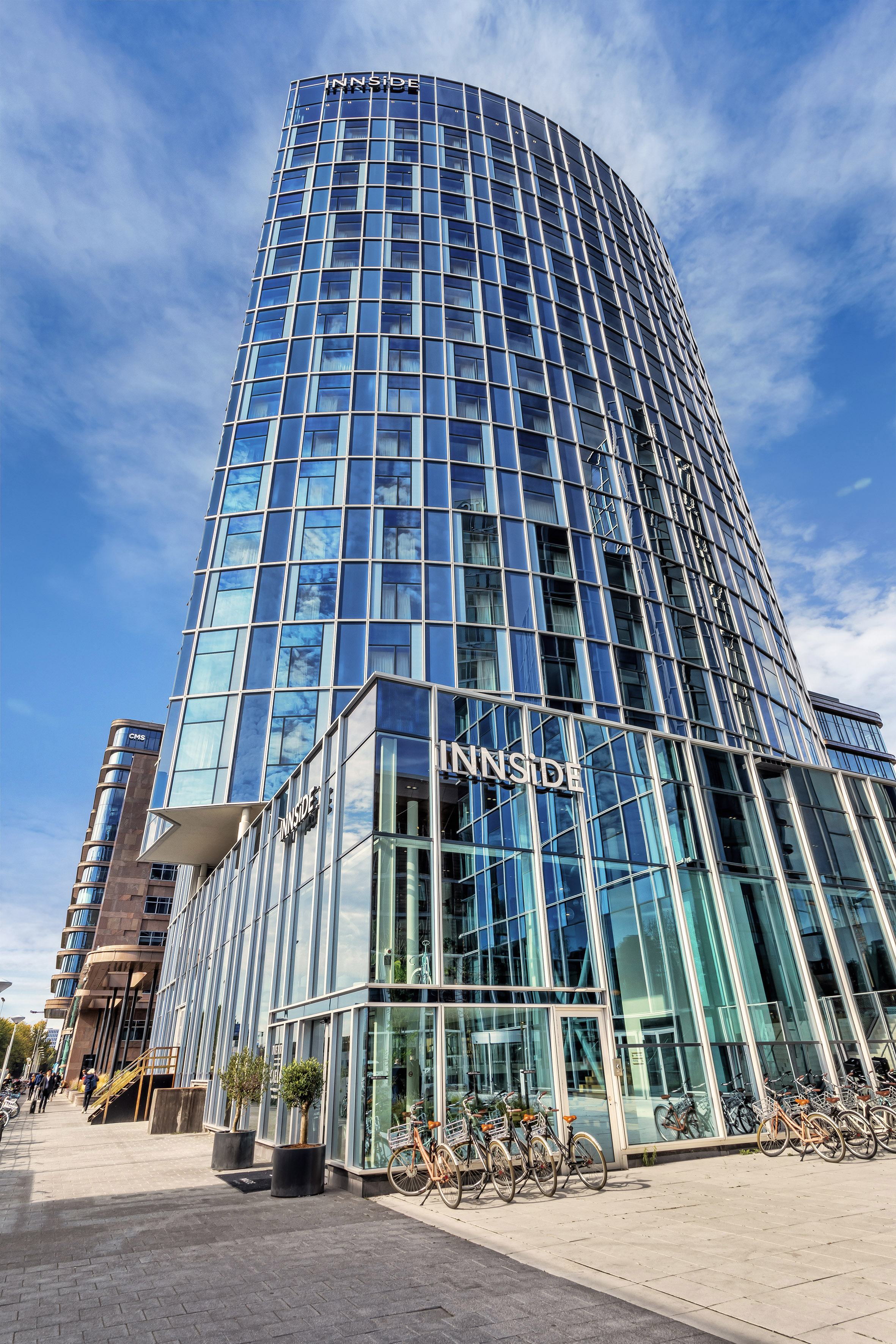 Modern INNSiDE hotel, curved glass facade reflecting blue sky, bikes parked.