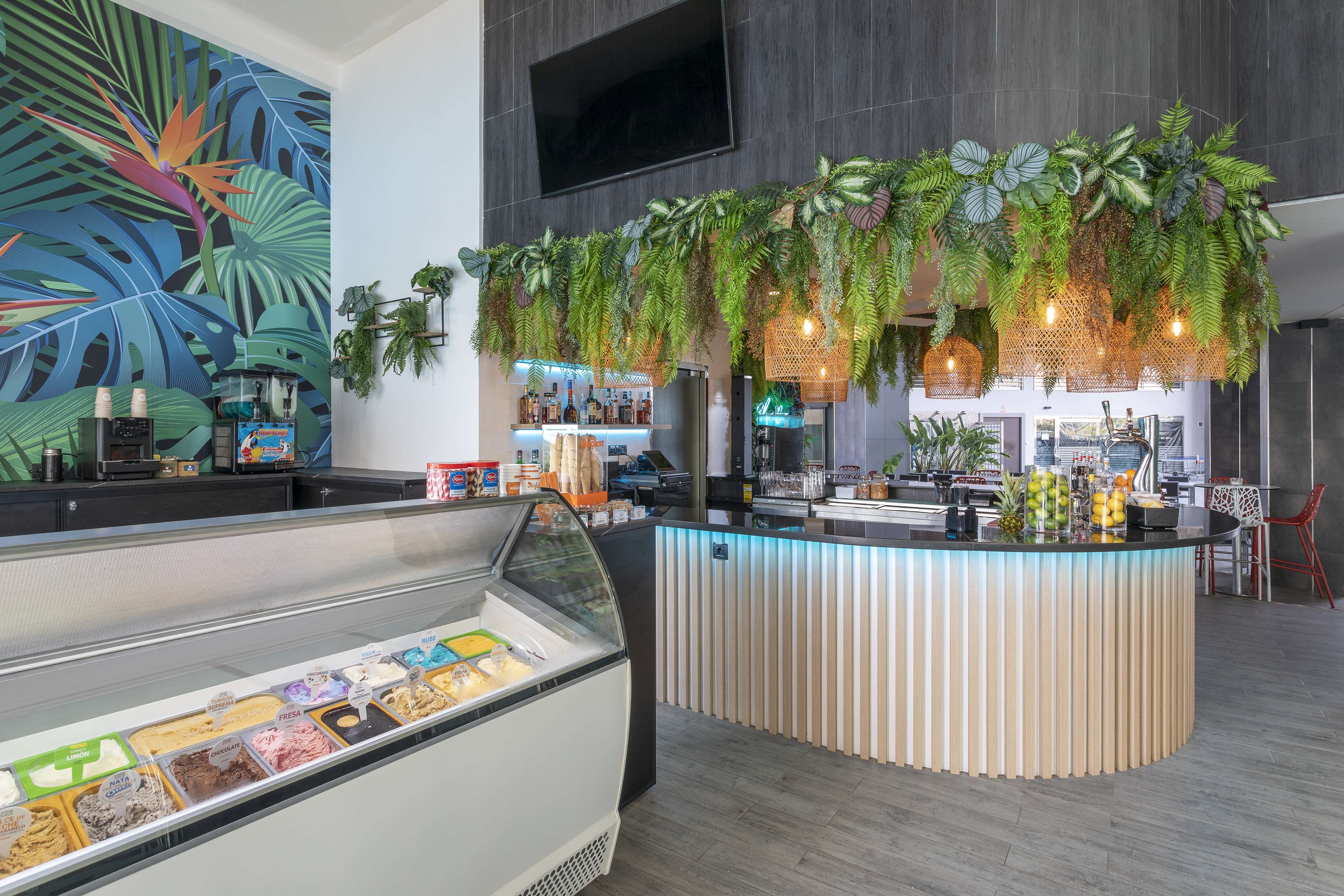 Tropical ice cream bar with illuminated counter, diverse gelato, and lush plant decor.
