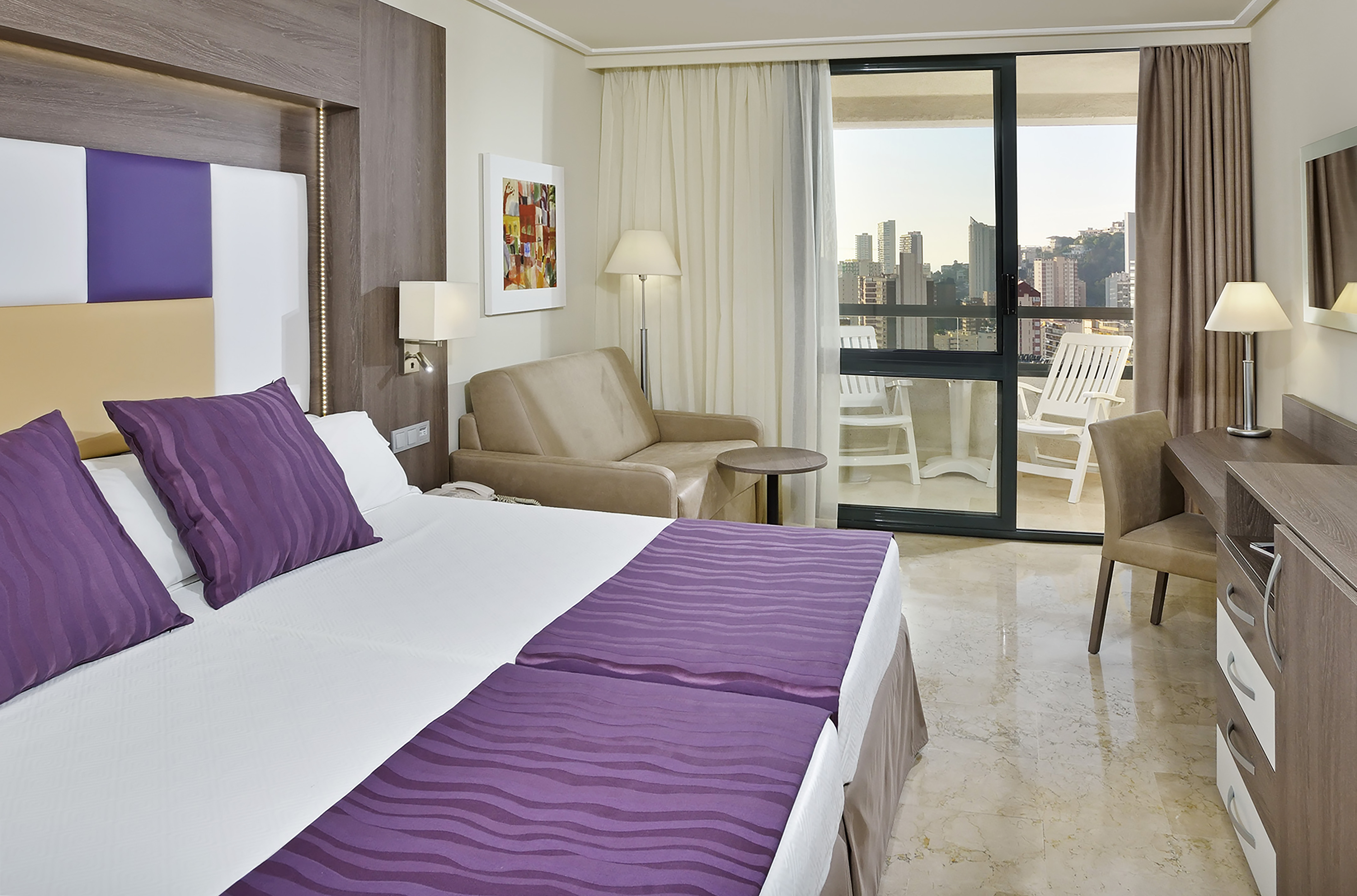 Hotel room with purple twin beds, balcony city view, and modern design.