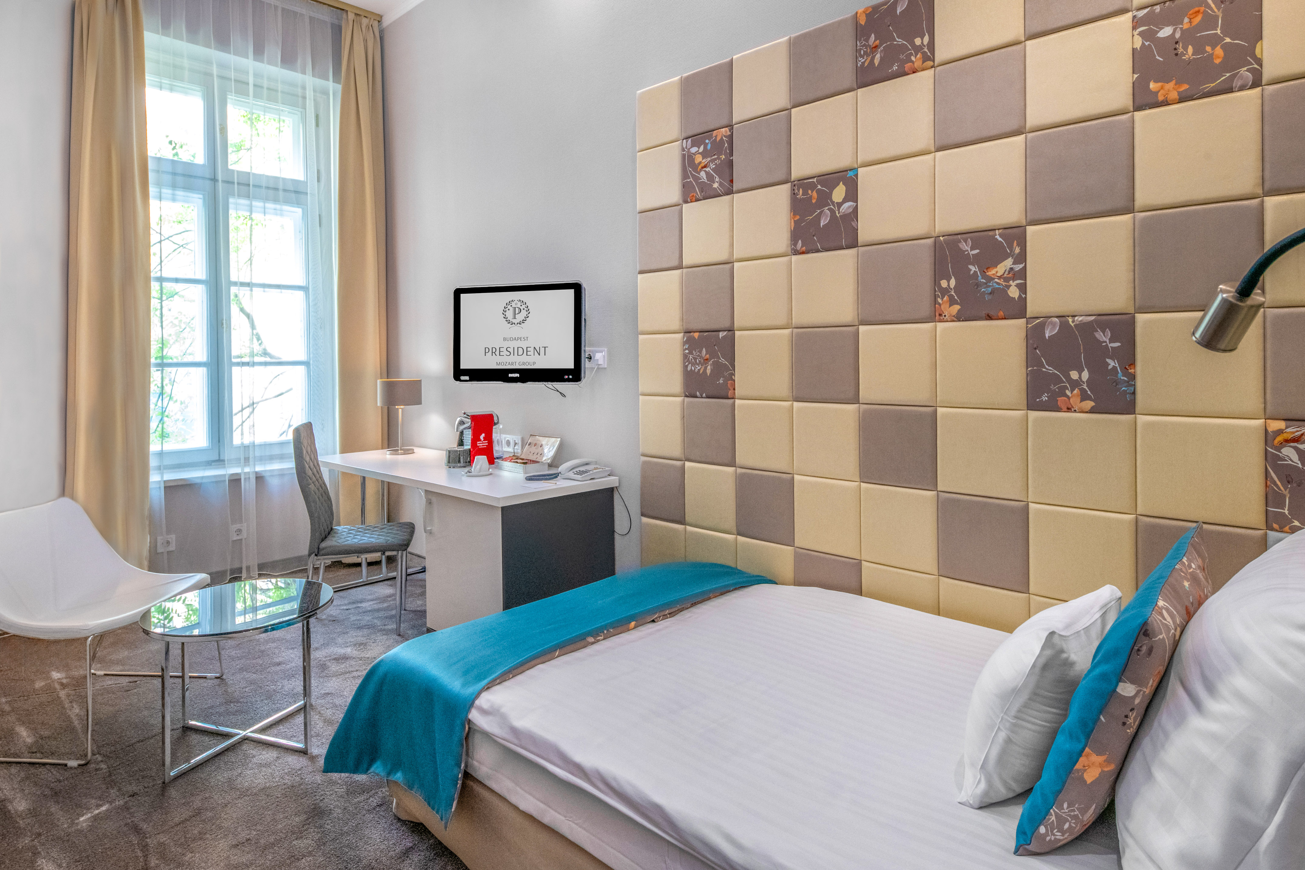 President Budapest hotel room with single bed, padded headboard, desk, and window.