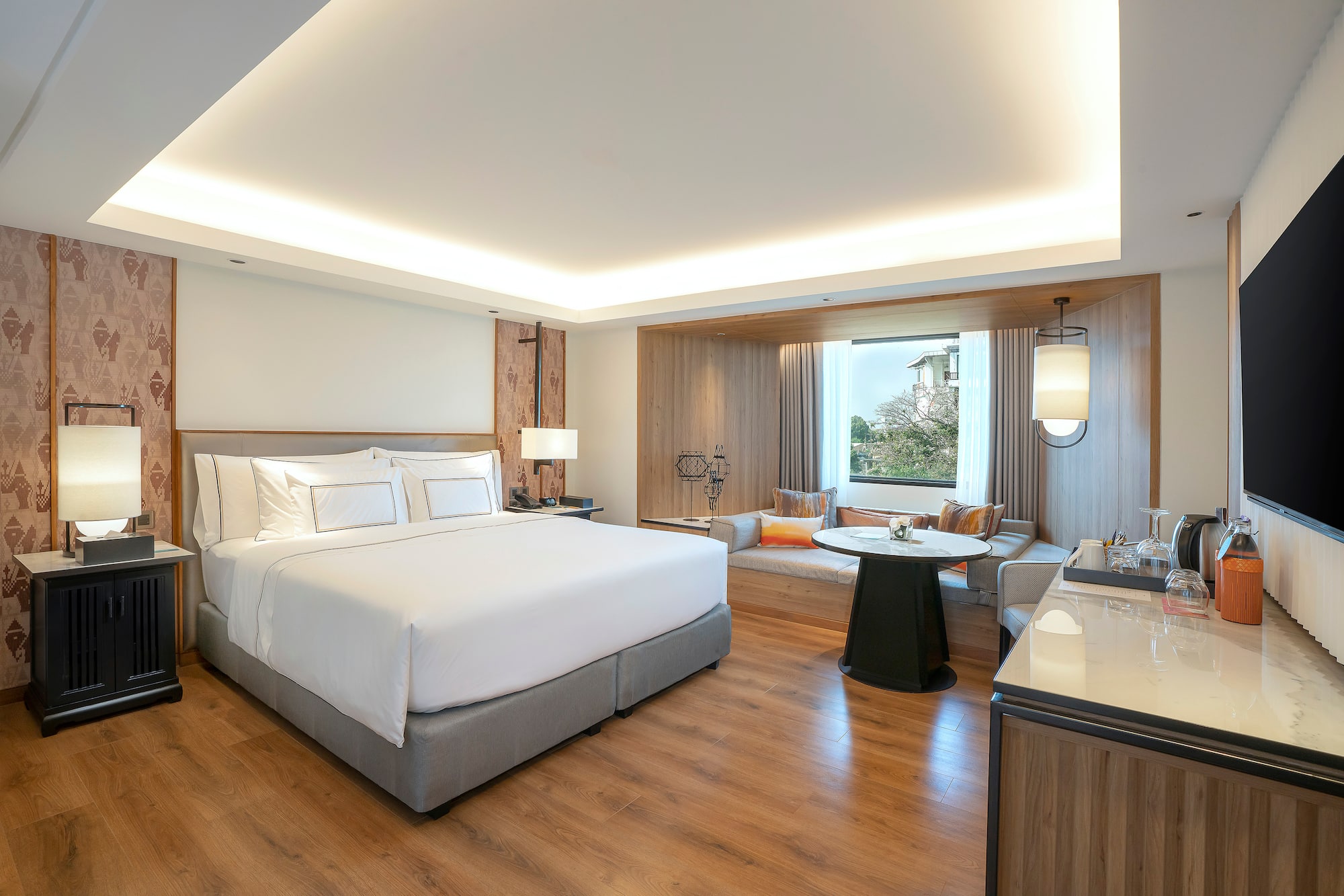Modern hotel bedroom interior with king bed, wood floors, and window lounge area.