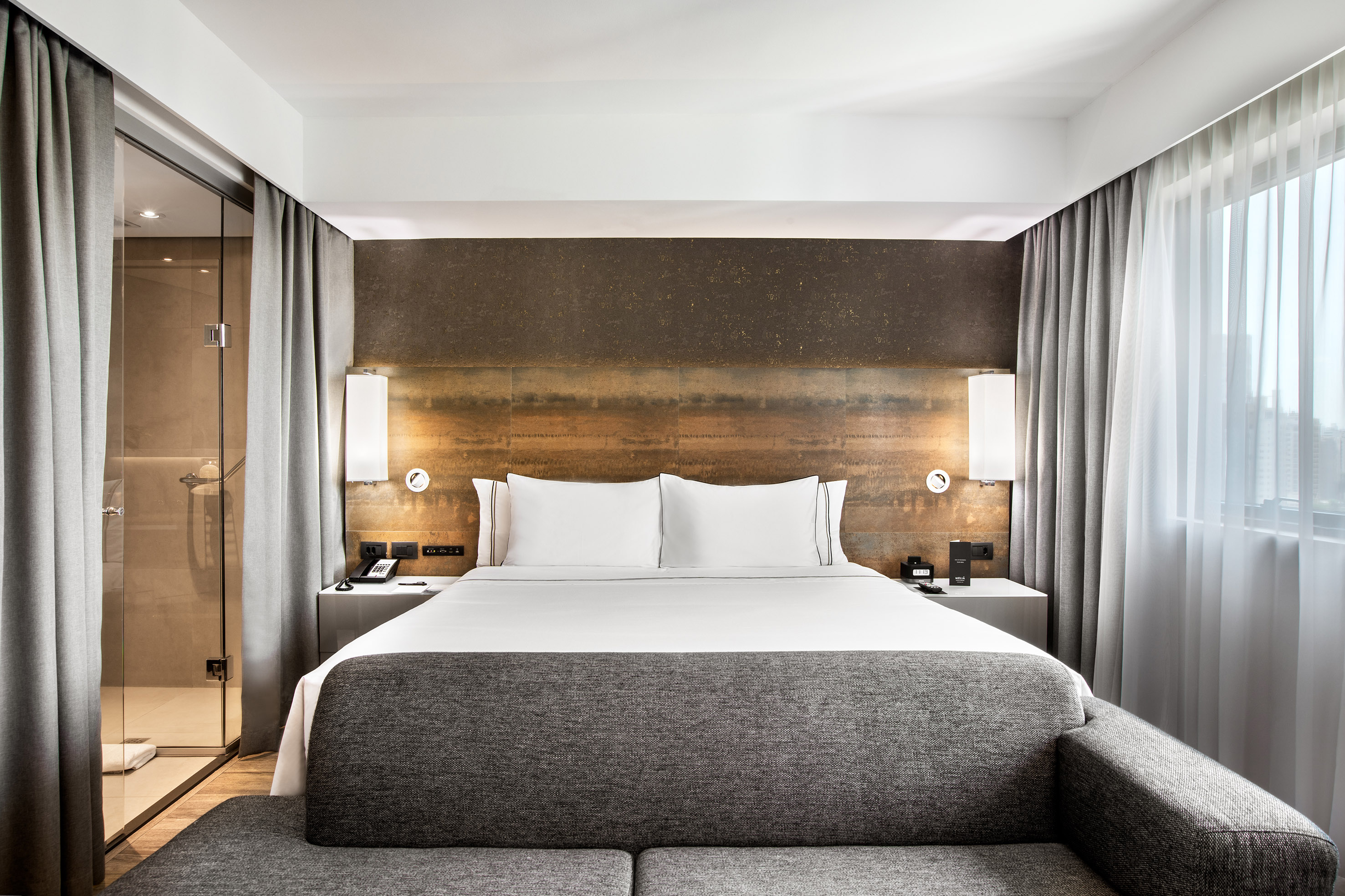 Contemporary hotel room with king bed, stylish headboard, and sleek glass shower.