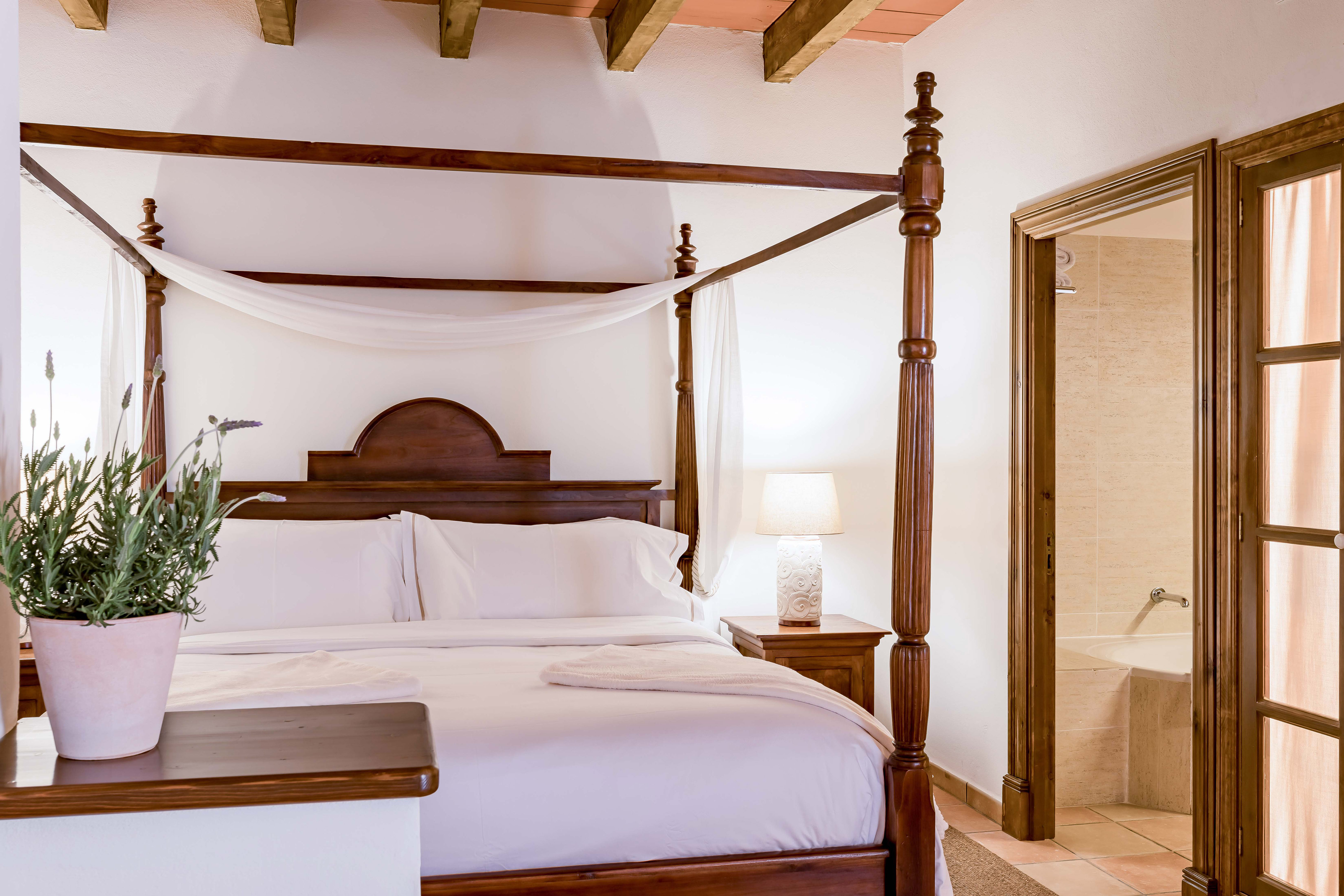 Rustic bedroom with wooden four-poster bed, white linens, and exposed beams.