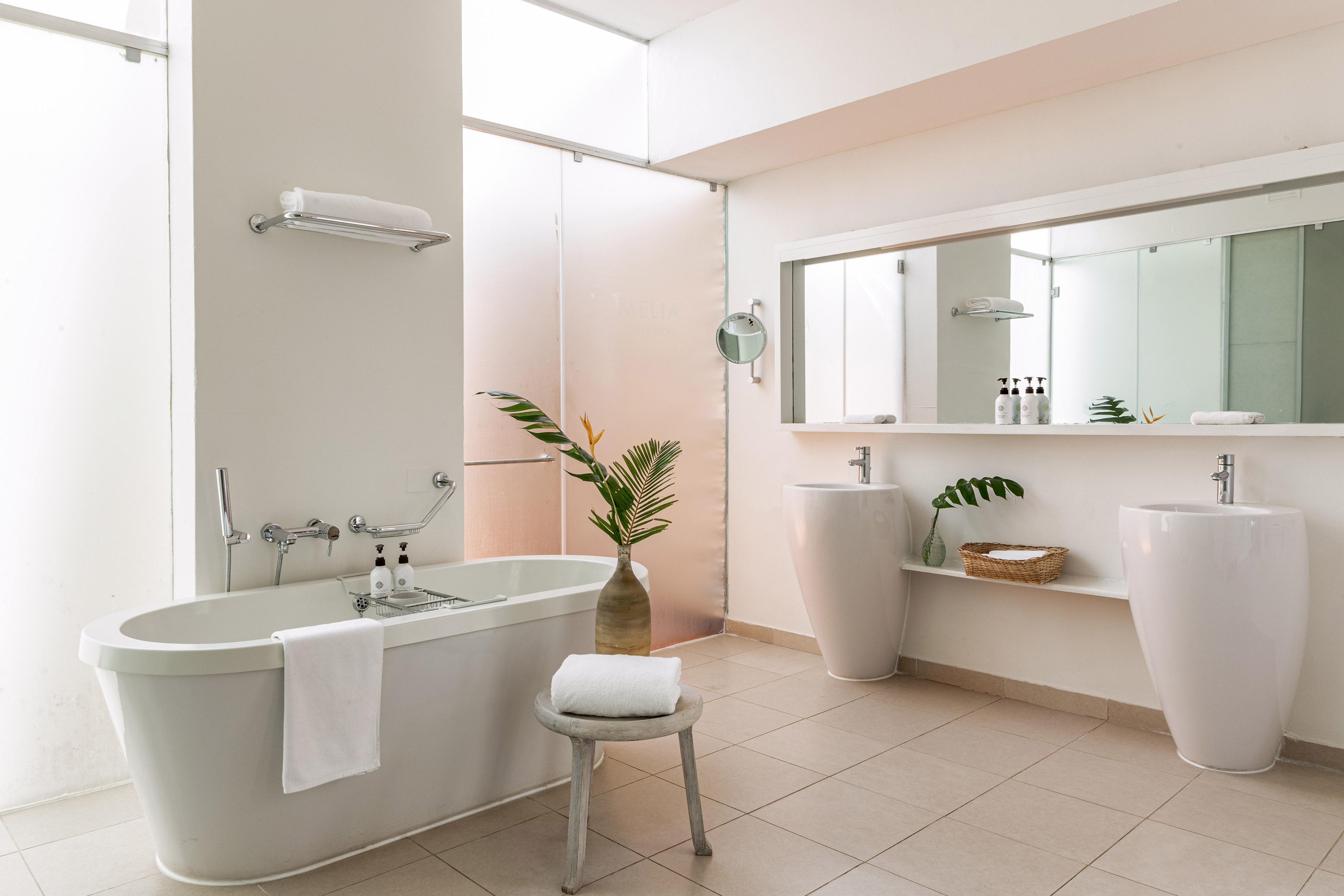 White modern bathroom with freestanding tub, dual sinks, and tropical decor.
