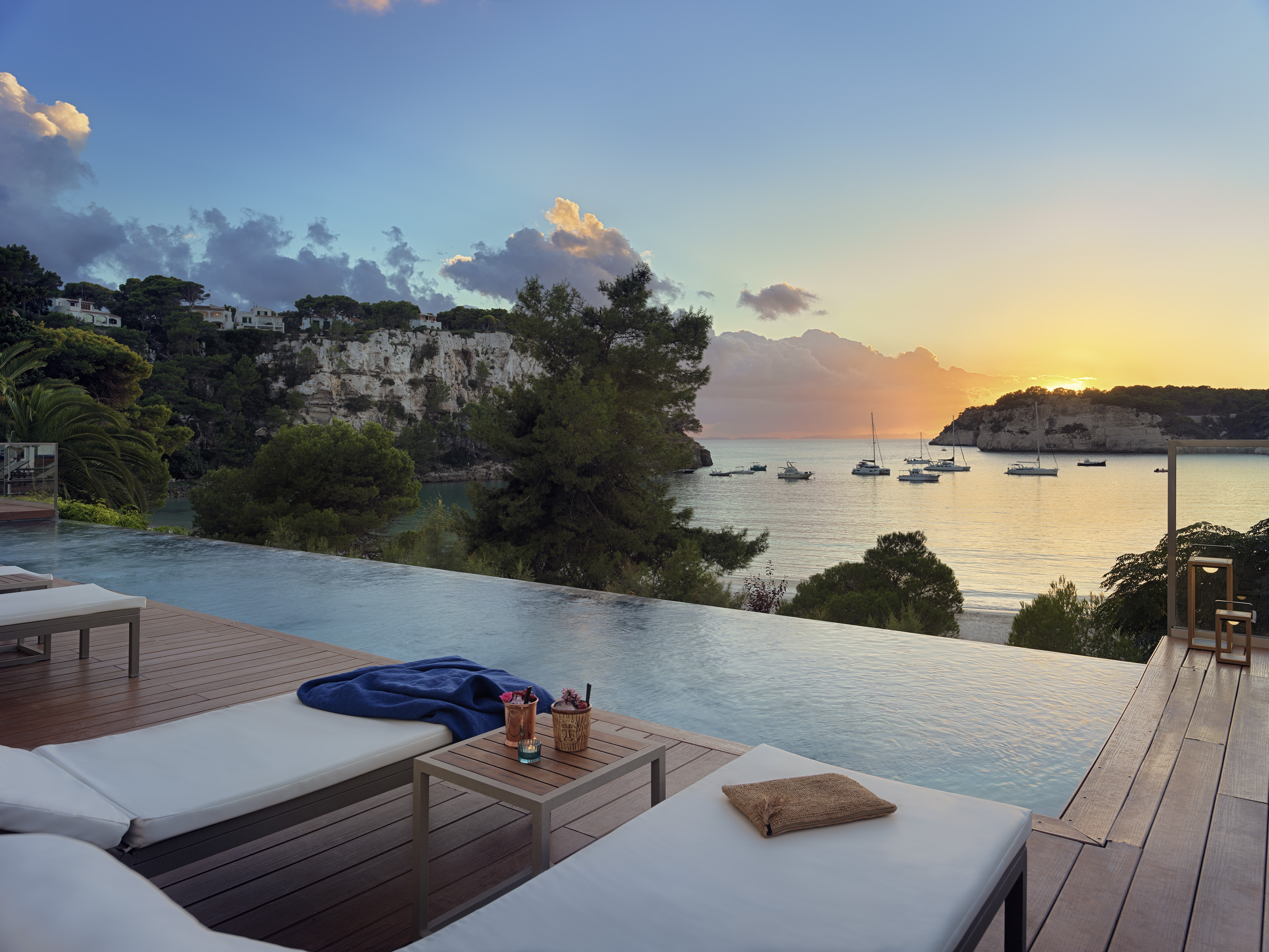 Luxury infinity pool at sunset overlooking coastal bay with boats.