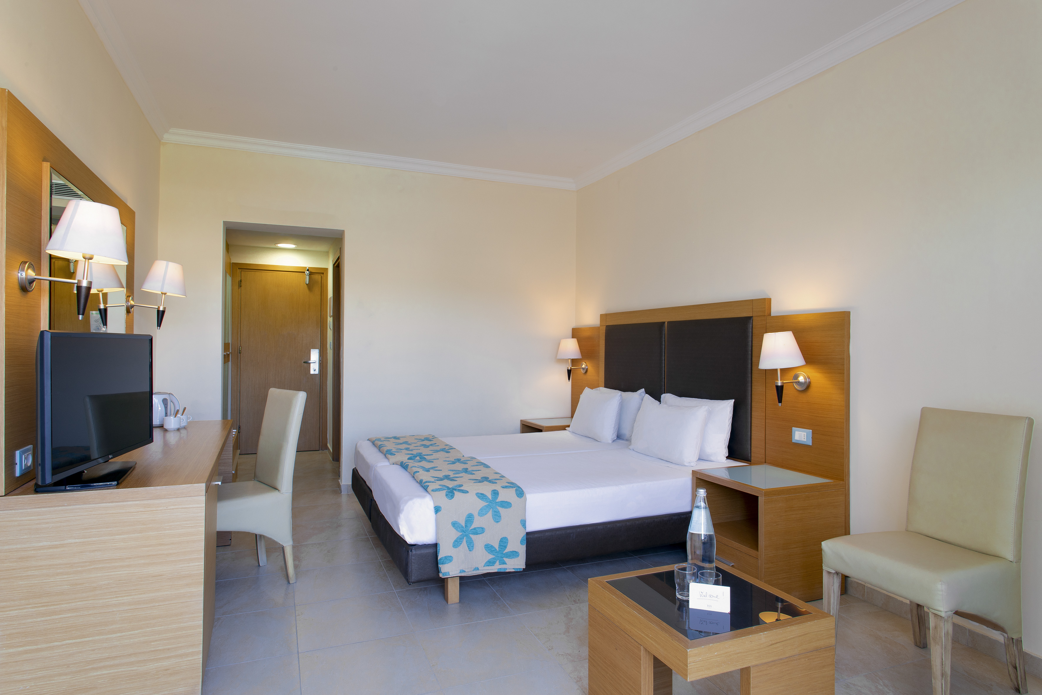 Hotel guest room with twin beds, wooden desk, TV, and modern decor.