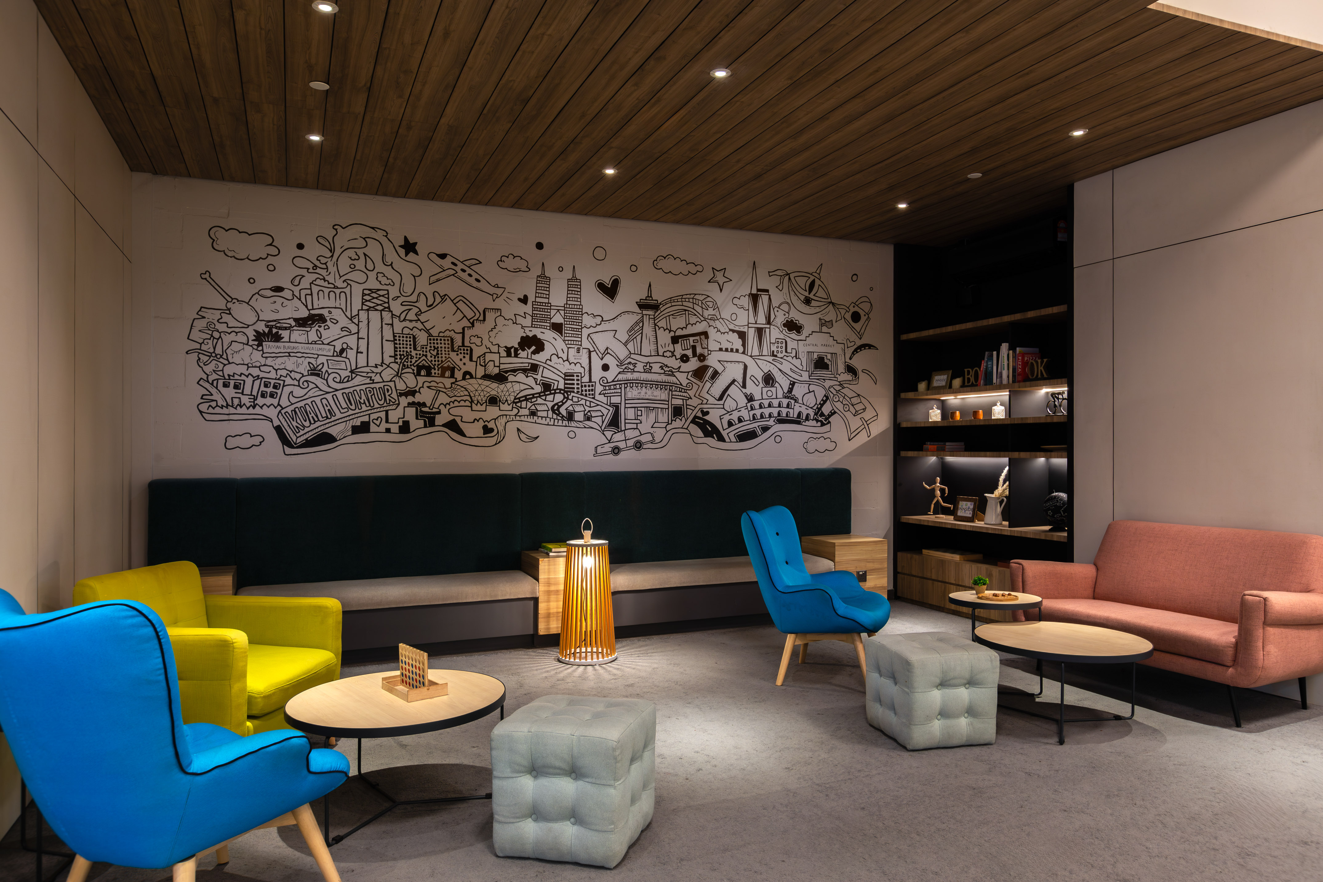 Modern lobby with Kuala Lumpur mural, vibrant seating, and wooden ceiling.