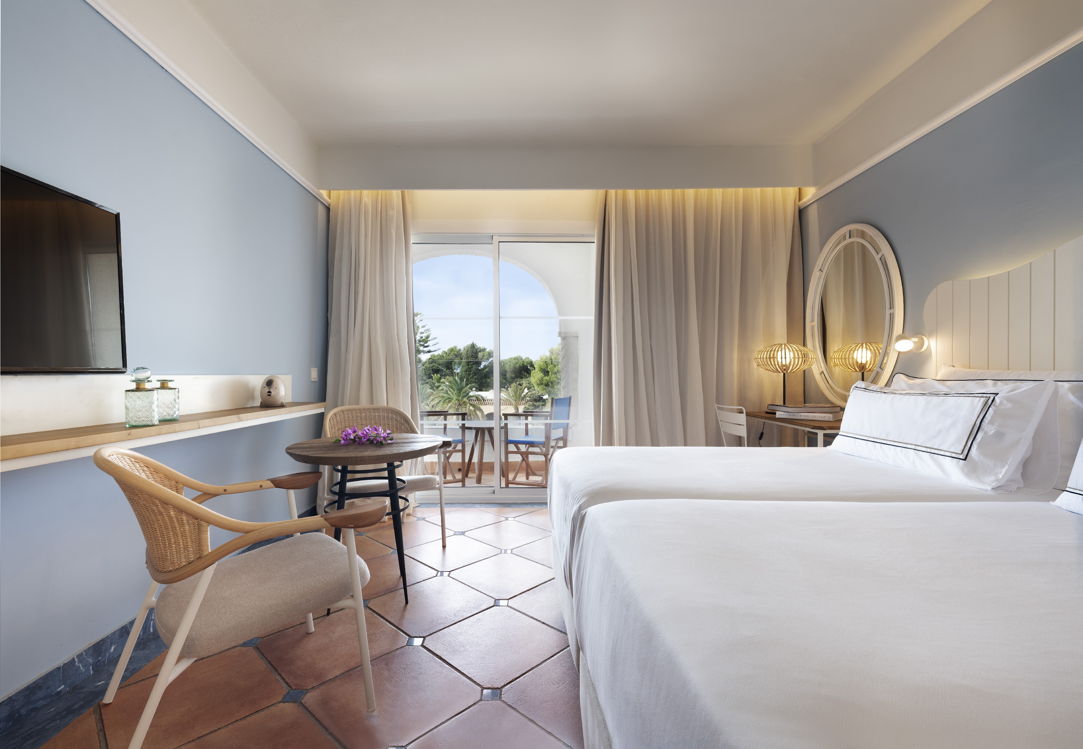 Bright hotel room with twin beds, balcony view, and Mediterranean style.