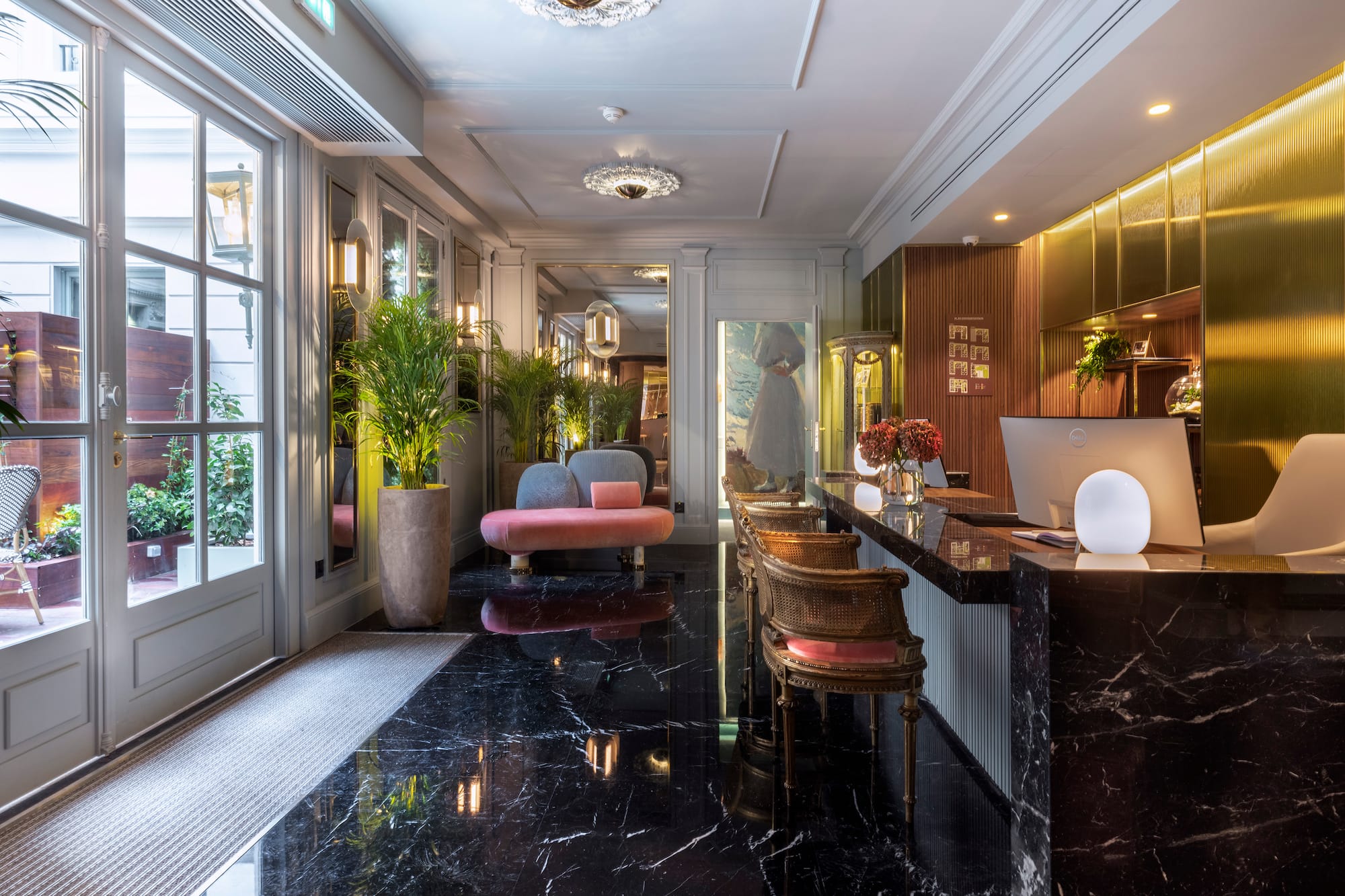 Elegant hotel lobby with black marble floor, gold reception desk, and pink lounge sofa.
