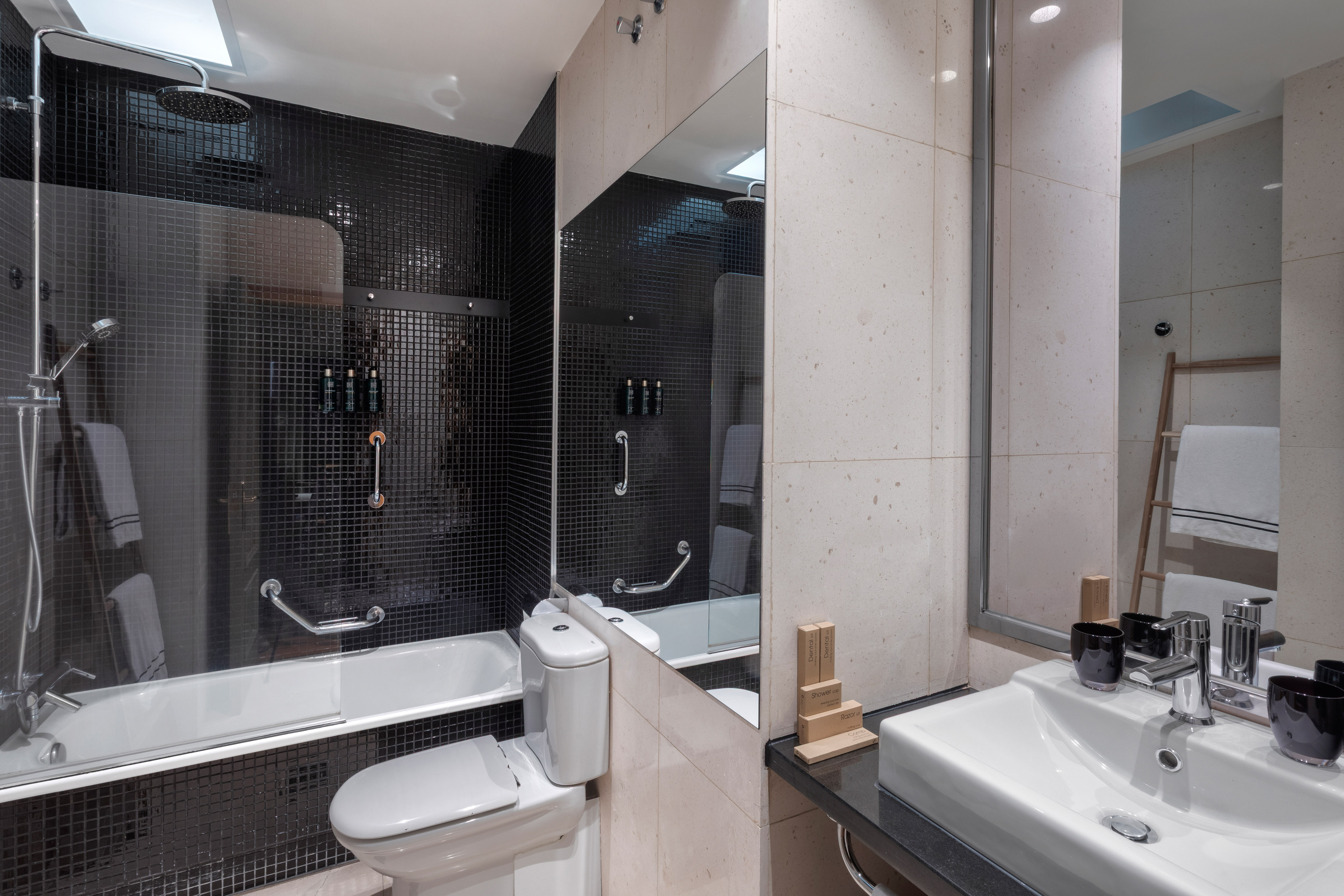 Modern bathroom with black mosaic tiled shower, white bathtub, toilet, and sink.