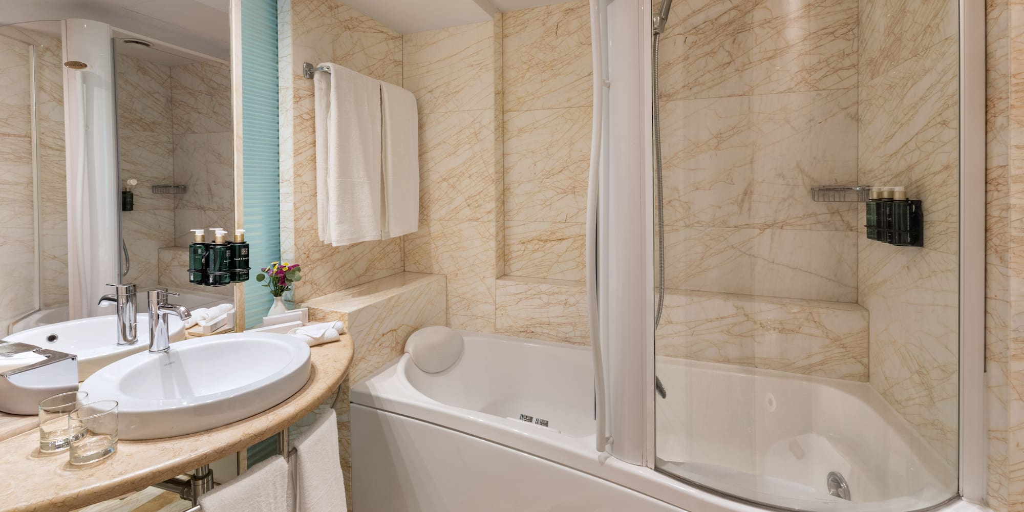 Luxury hotel bathroom with marble walls, bathtub, shower, and sink.