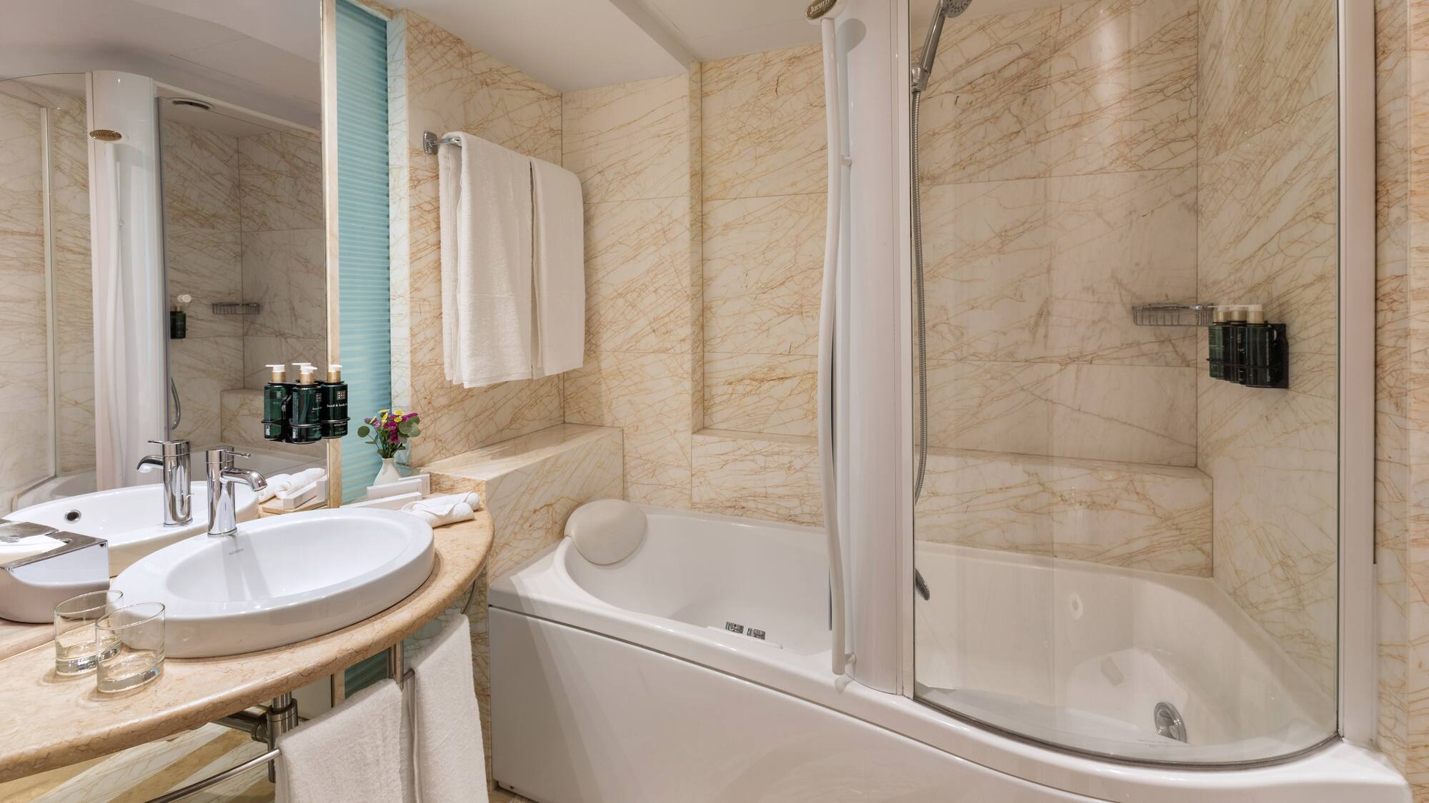 Luxury hotel bathroom with marble walls, bathtub, shower, and sink.