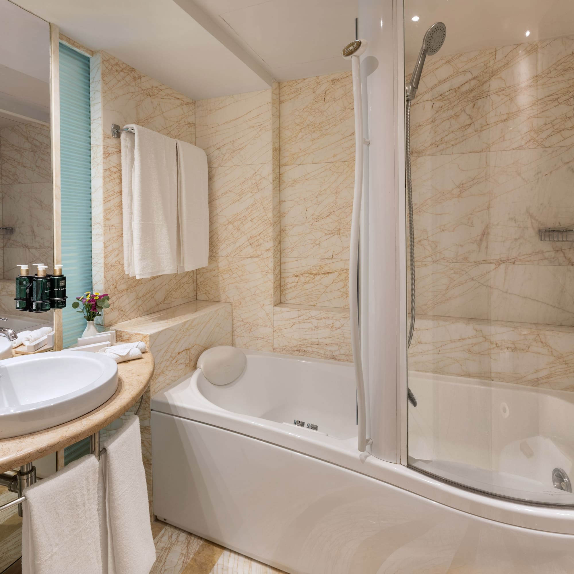 Luxury hotel bathroom with marble walls, bathtub, shower, and sink.